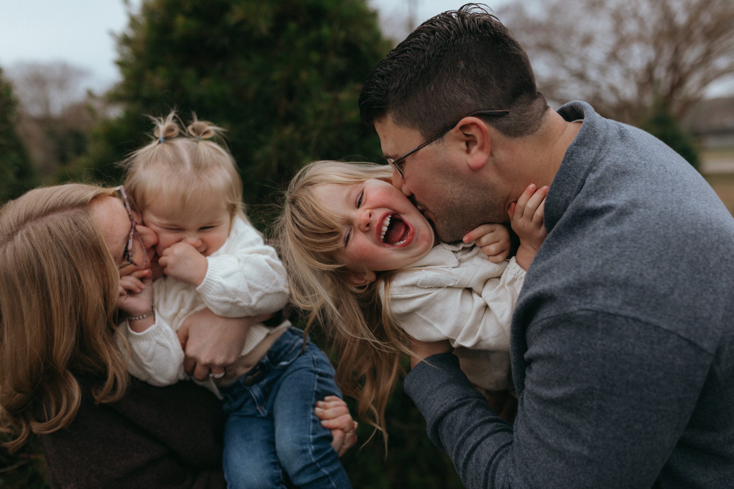 Family of four outdoors, two children and two adults, smiling and laughing together.