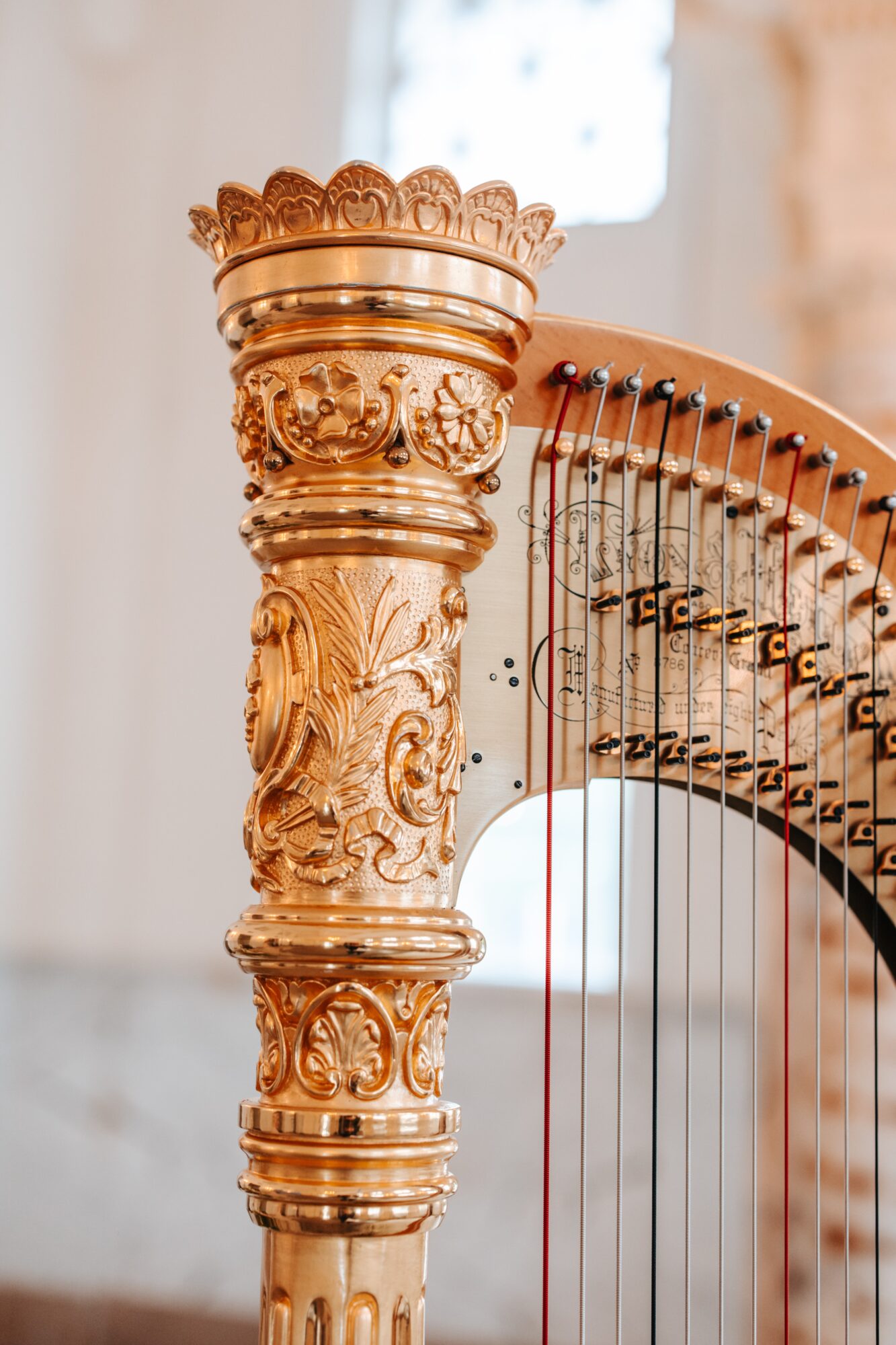 Close-up of an ornate, gold-colored column with intricate carvings, part of a harp, and a blurred background.