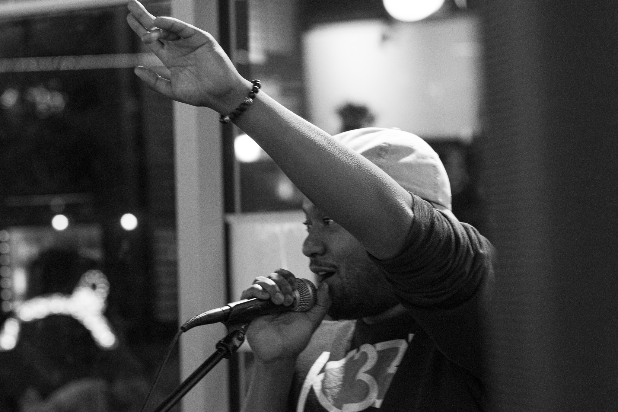 Person singing into microphone with arm raised, wearing a cap, indoors at night, black and white photo.