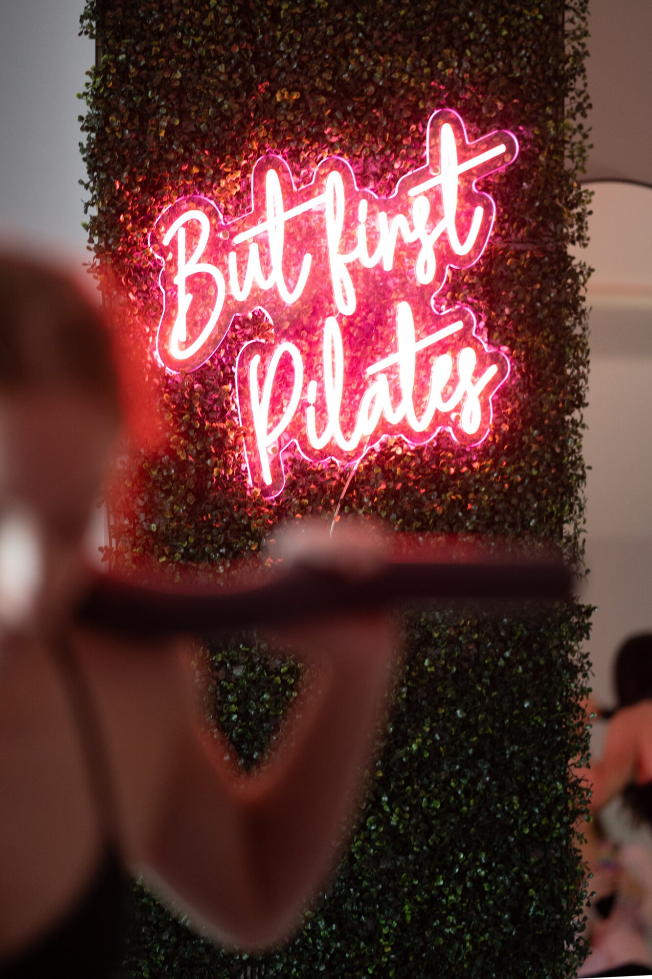 Pink neon sign reads 'But First Plates' against a green leafy background.