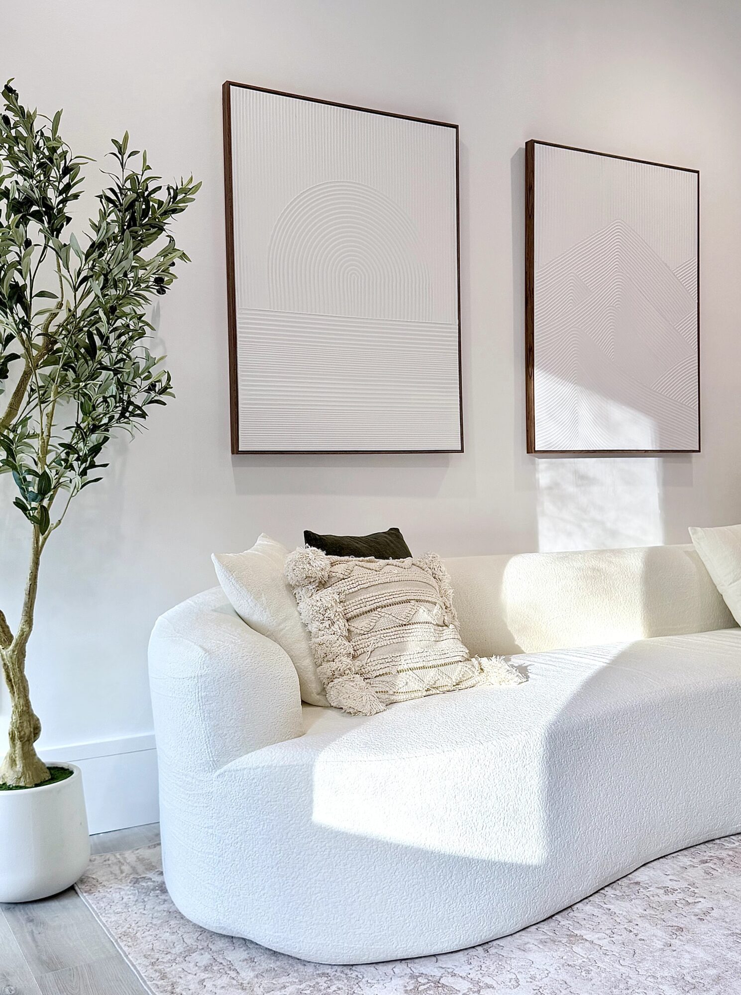 Living room with white sofa, decorative pillows, wall art, and a potted plant, bright and modern decor.