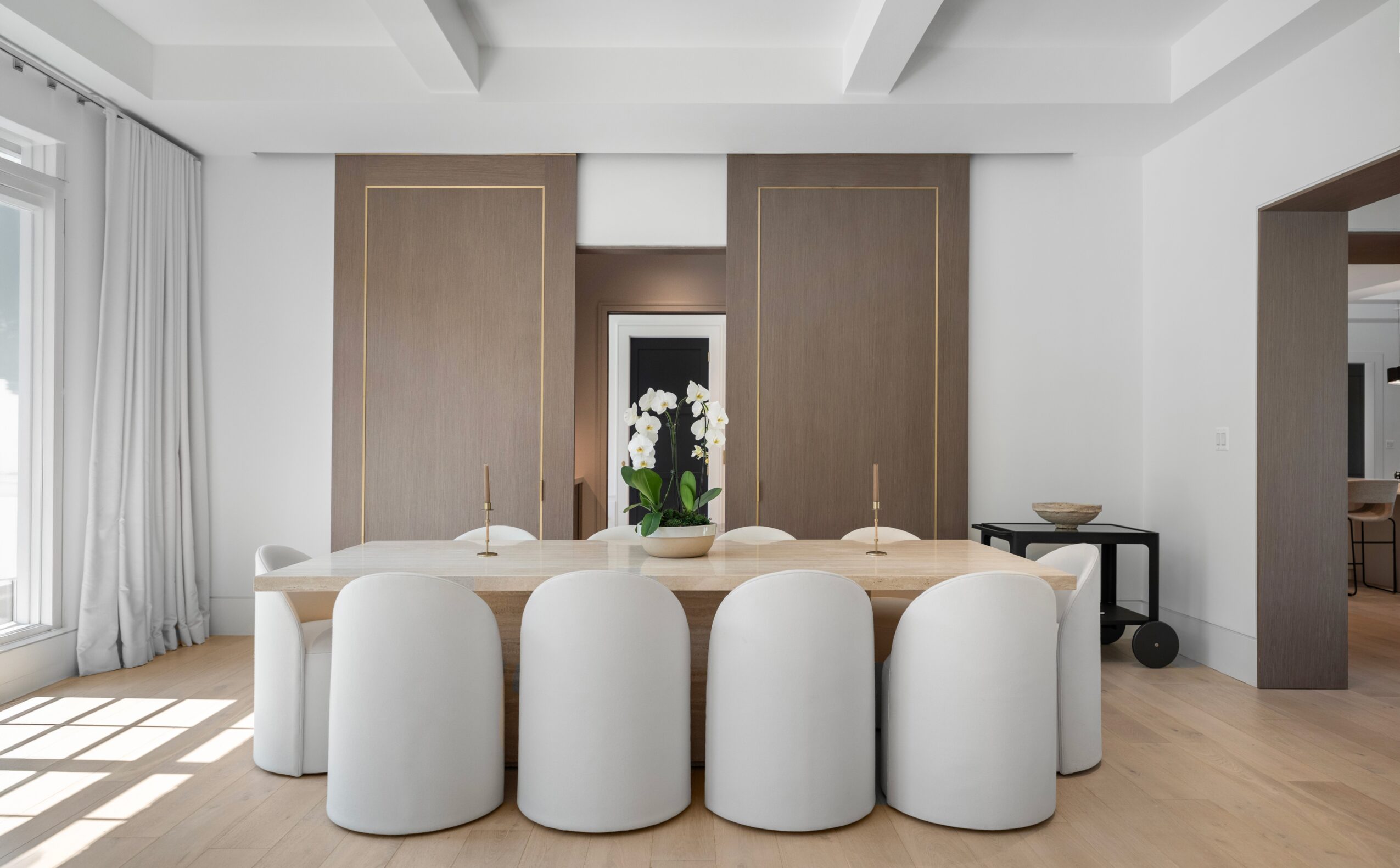 Modern dining room with a large oval table, white chairs, and a decorative centerpiece, bright with natural light.