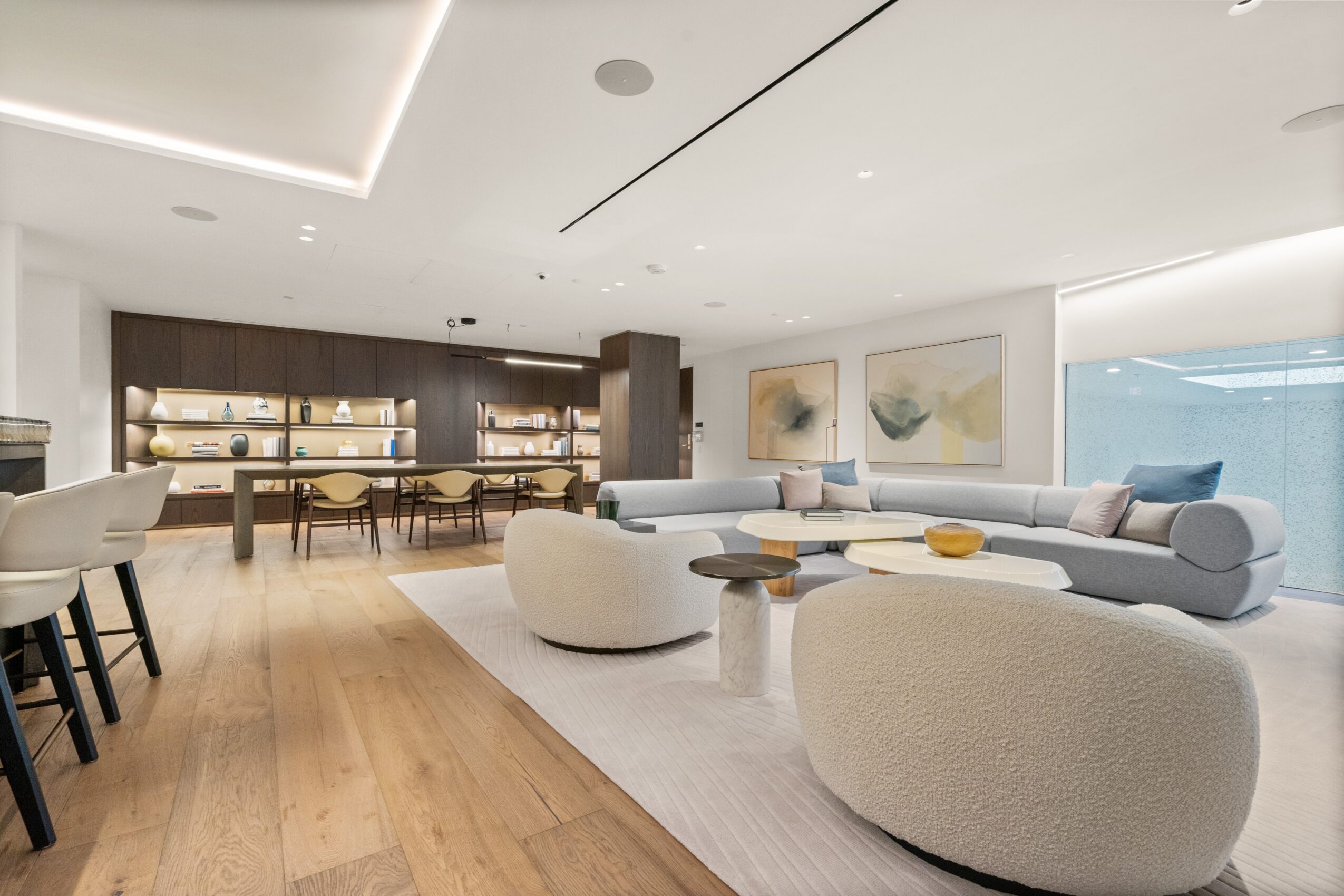 Modern living room with white sofa, round ottomans, artwork, and wooden flooring, bright and spacious interior.