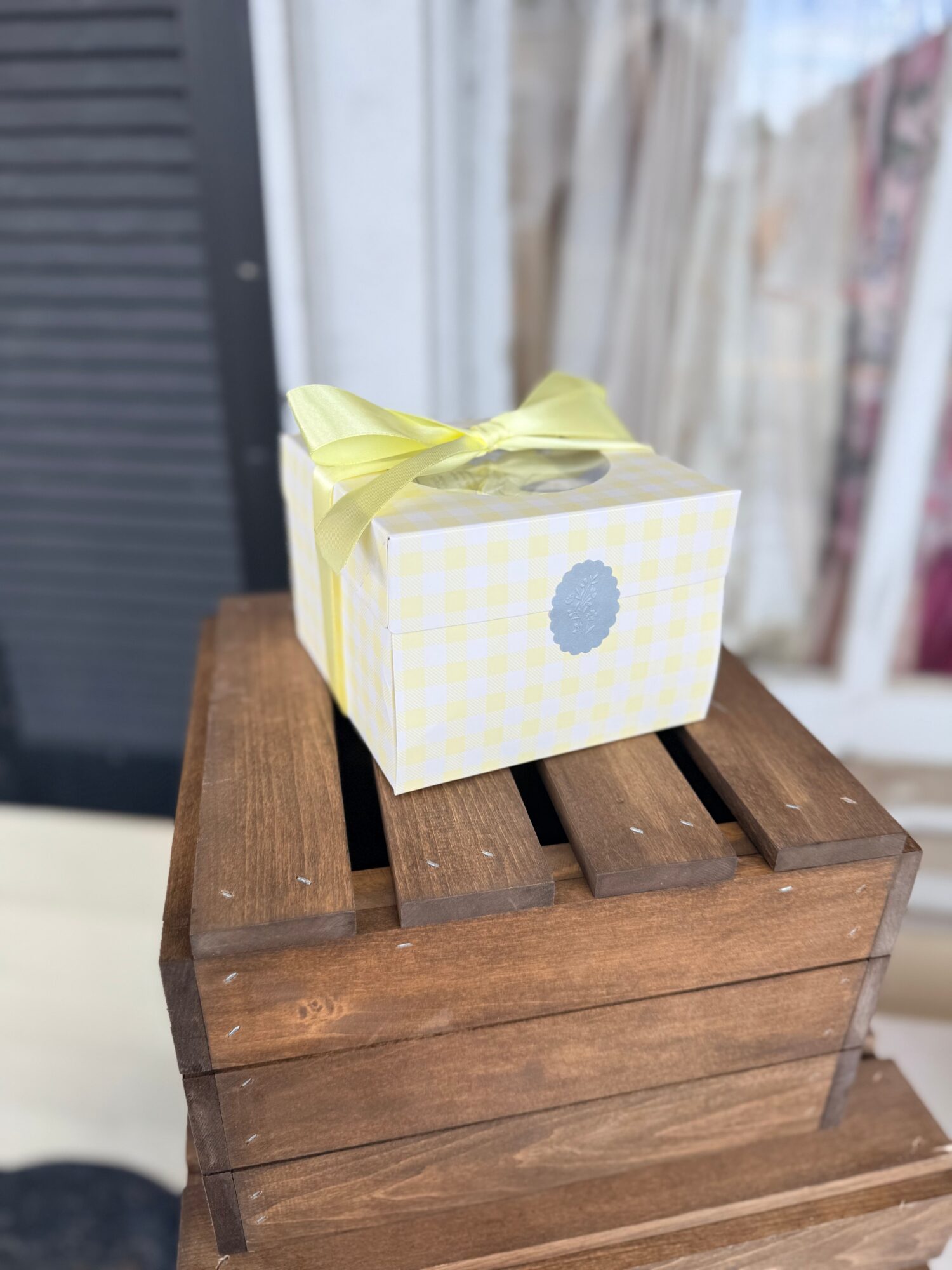 Small gift box with yellow ribbon on wooden surface, background of window and outdoor scene.
