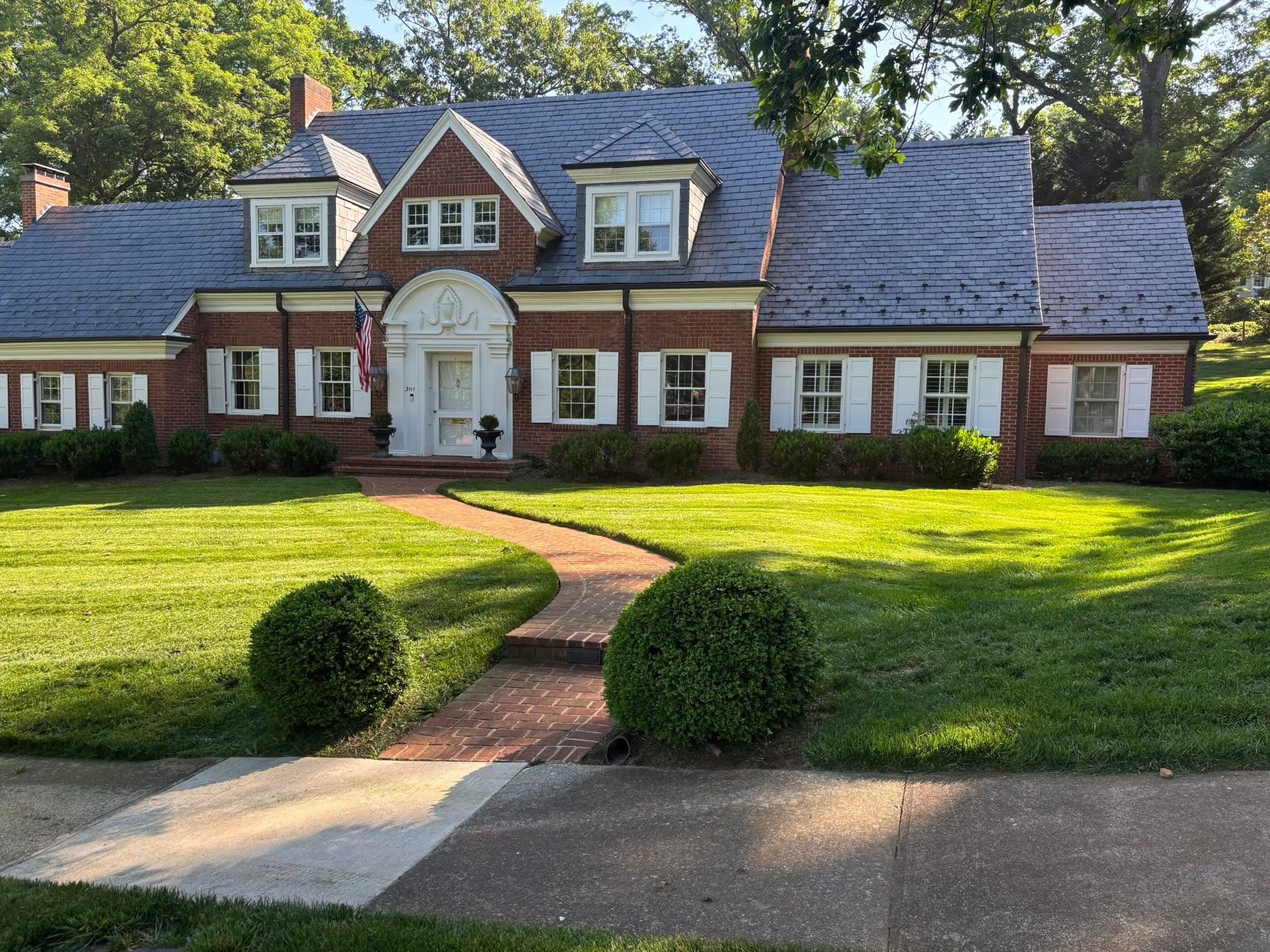 Large brick house with a curved walkway leading to the front door, surrounded by a green lawn and trees.