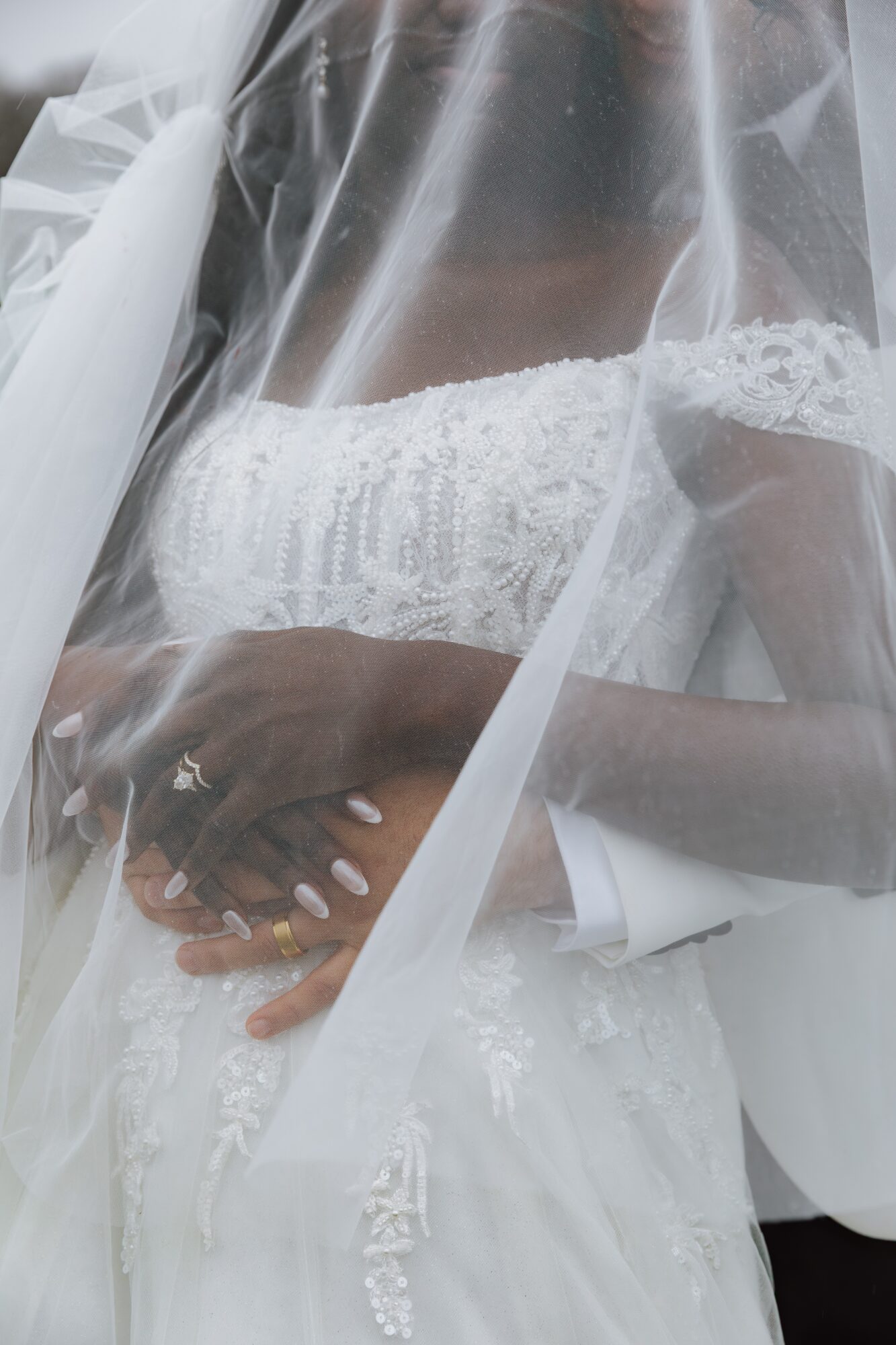 Close-up of a bride in a wedding dress with a veil, hands resting on her waist, lace details visible.