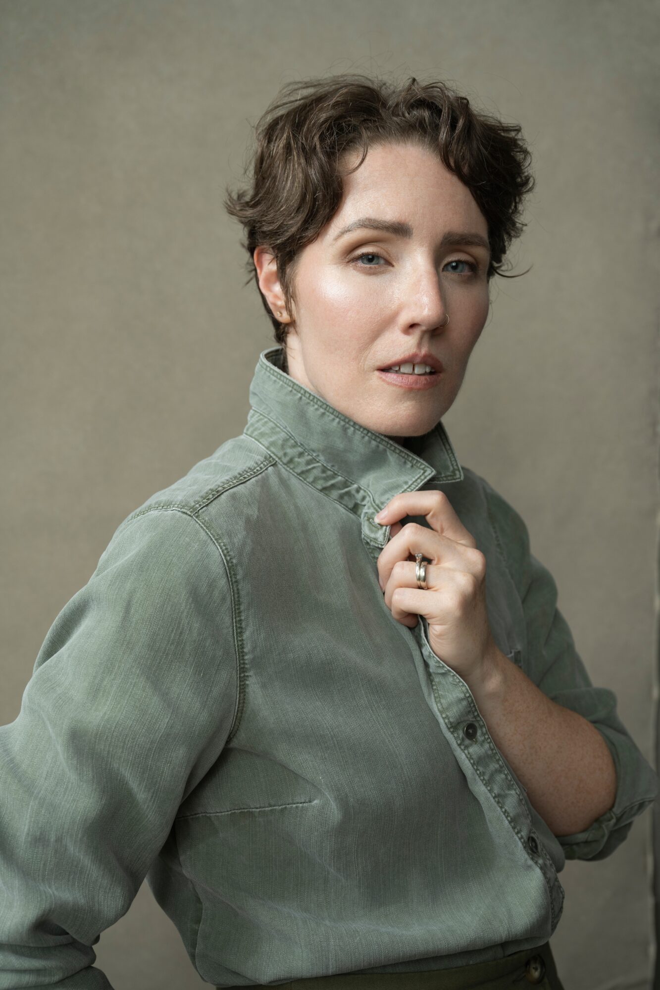 Woman with short, wavy hair wearing a green button-up shirt, looking at the camera with a neutral expression.