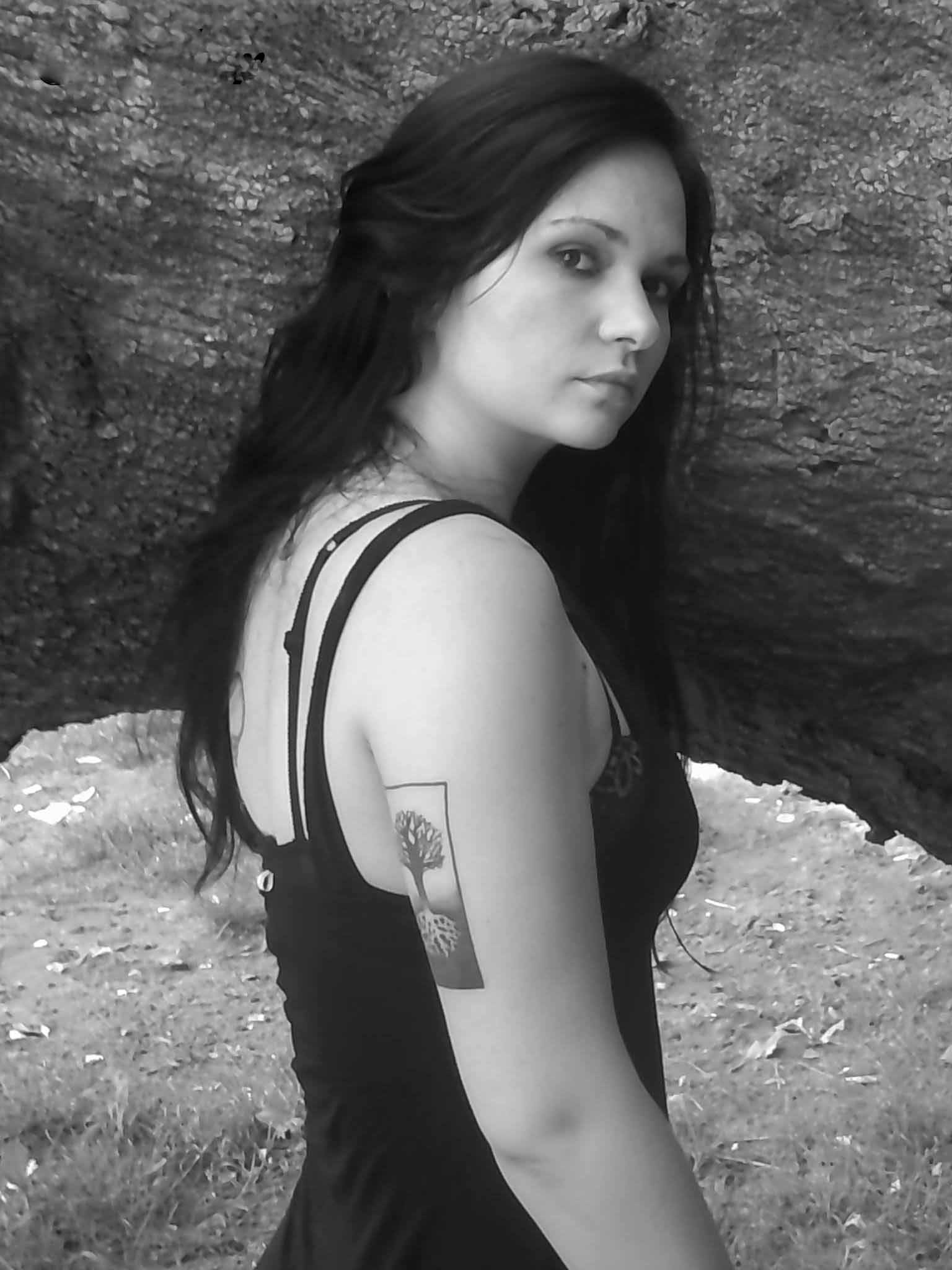 Young woman with long dark hair, wearing a sleeveless top, standing outdoors against a rocky background.