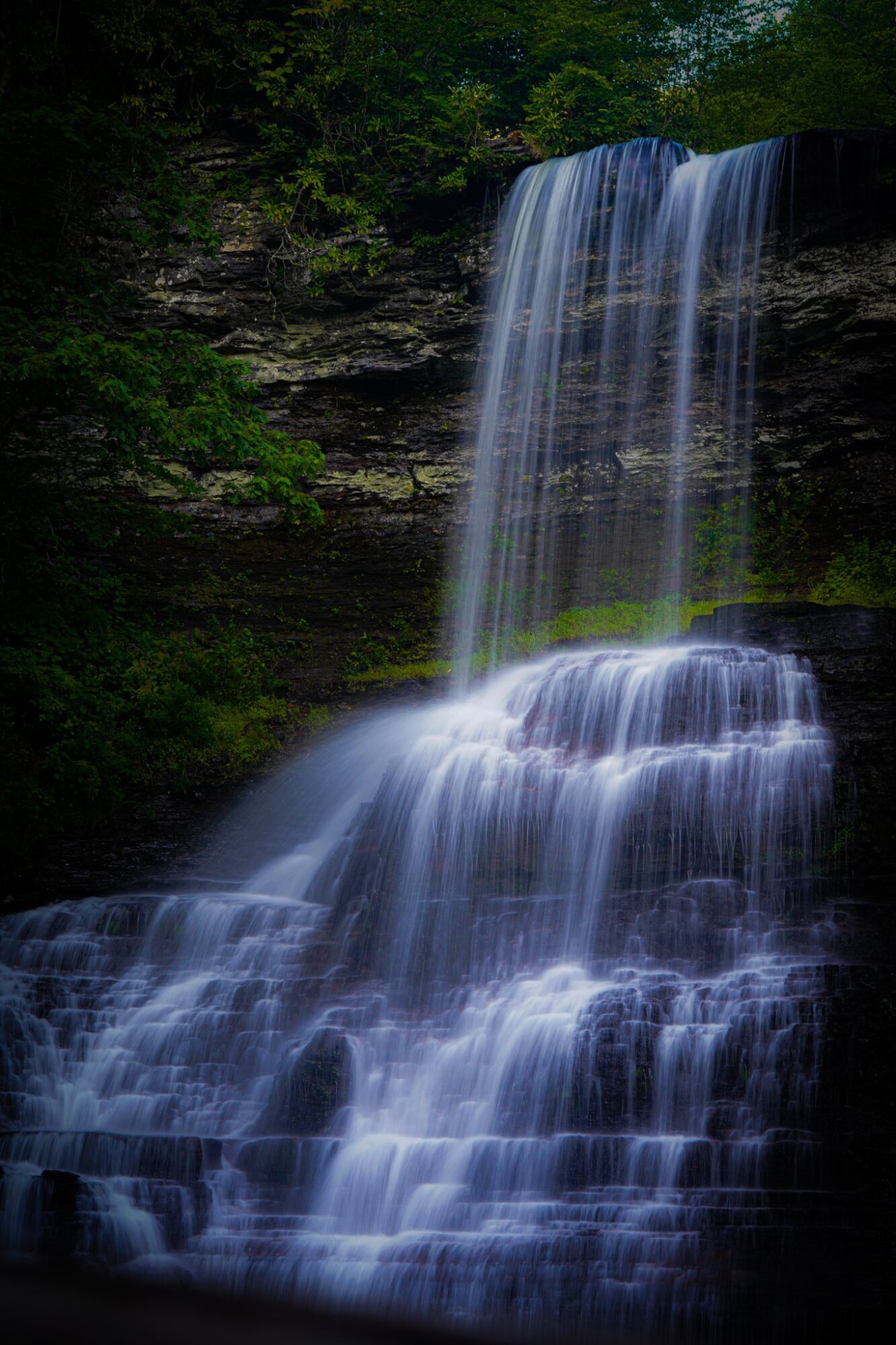 Waterfall cascading over rocks in a lush green forest, with water flowing down multiple levels.