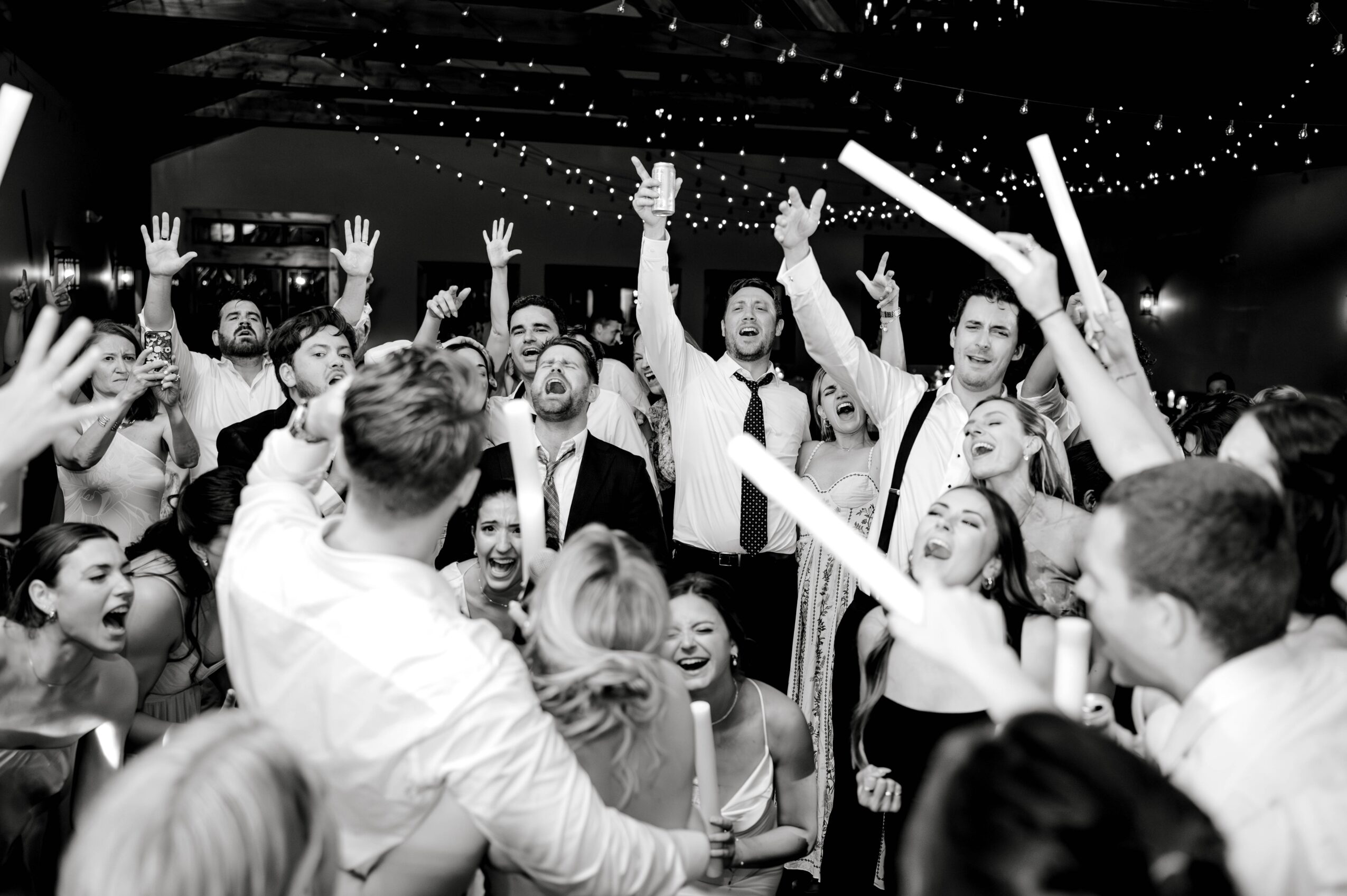 Group of people dancing and celebrating indoors with confetti and string lights overhead.