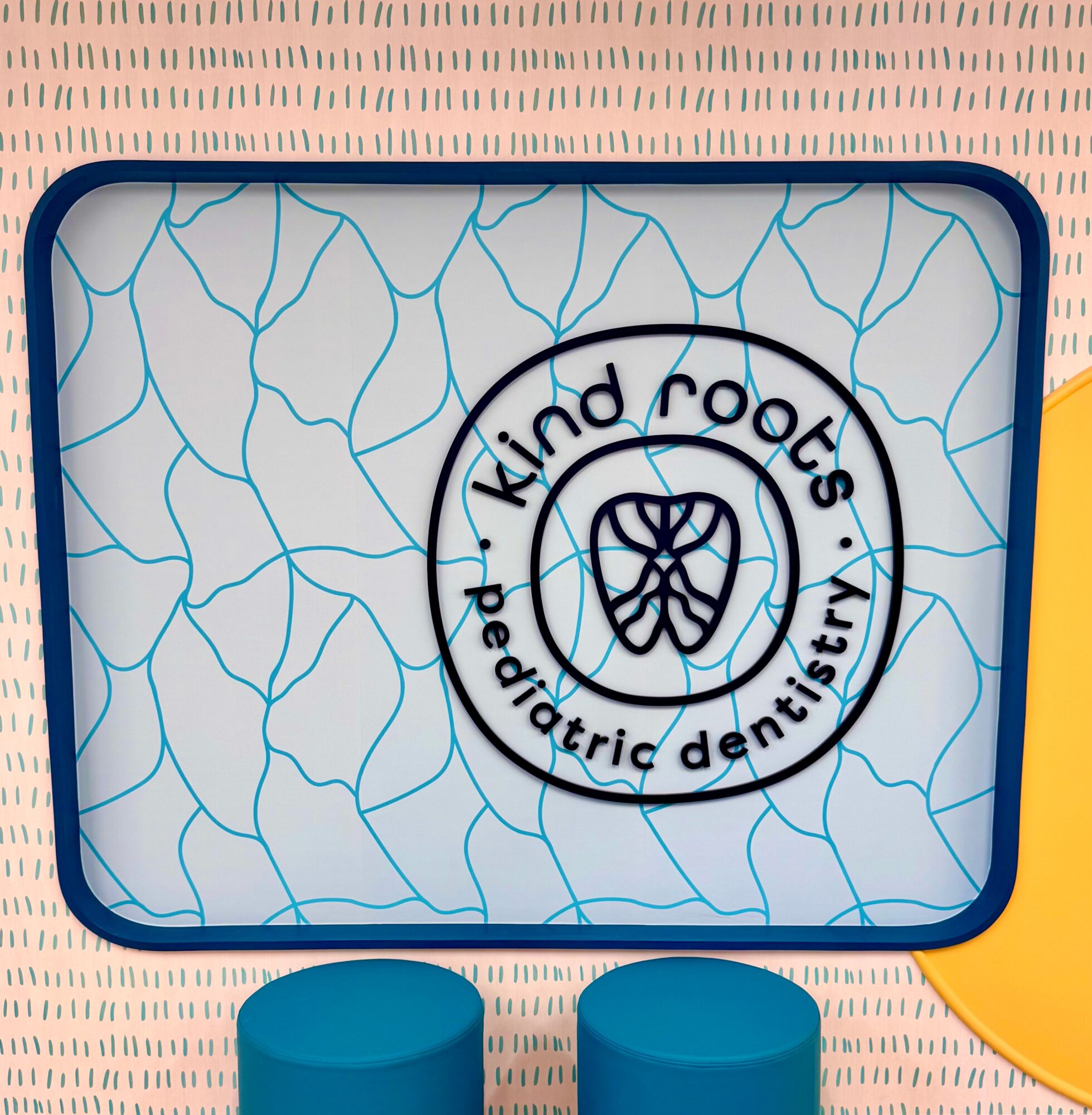 Sign with text 'kind roots pediatric dentistry' and a tooth logo, on a patterned background.