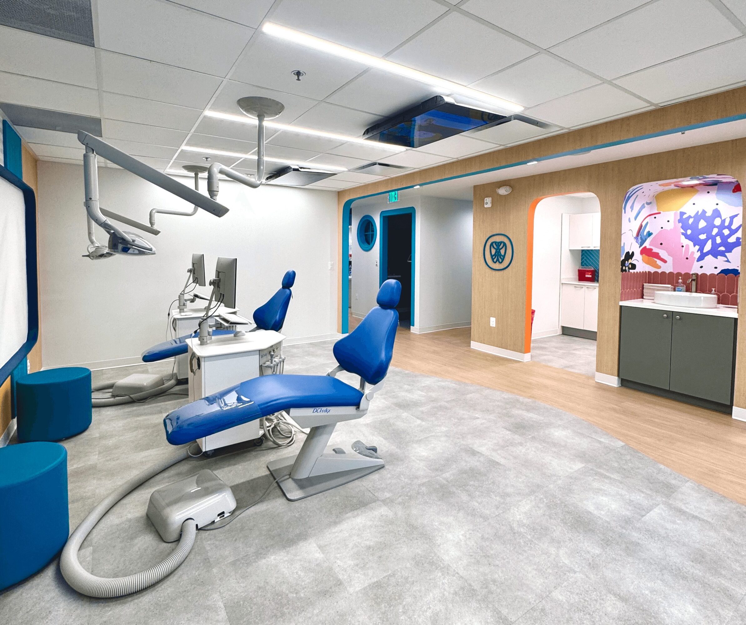 Dental clinic with chairs, equipment, and a colorful mural in the background, well-lit and clean environment.