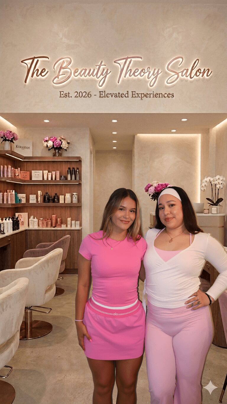 Two women stand inside a salon with shelves of products and flowers, smiling at the camera.