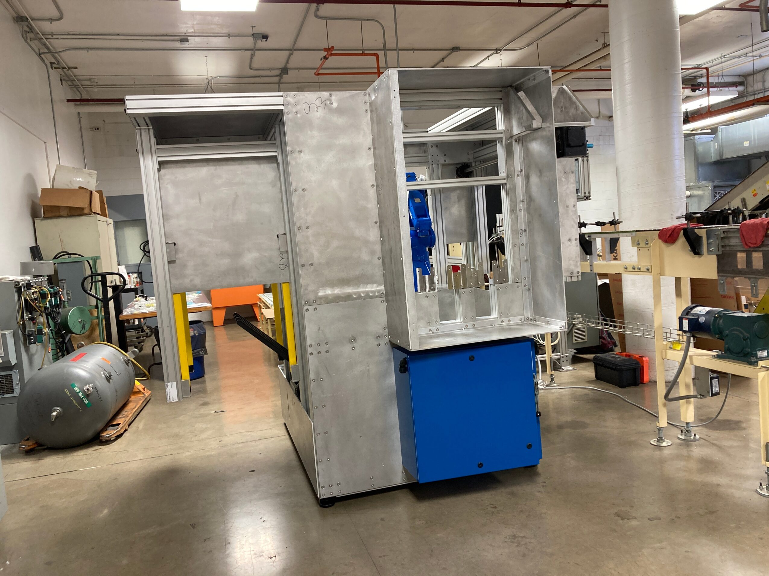 Metal enclosure with a blue panel, situated in an industrial workshop with tools and equipment around.