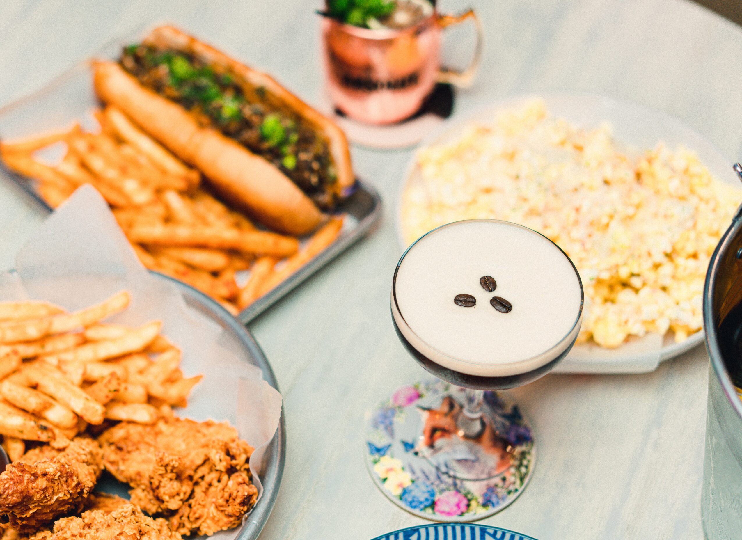Assorted foods including a hot dog with green relish, fries, fried chicken, a bowl of rice, and a drink on a table.