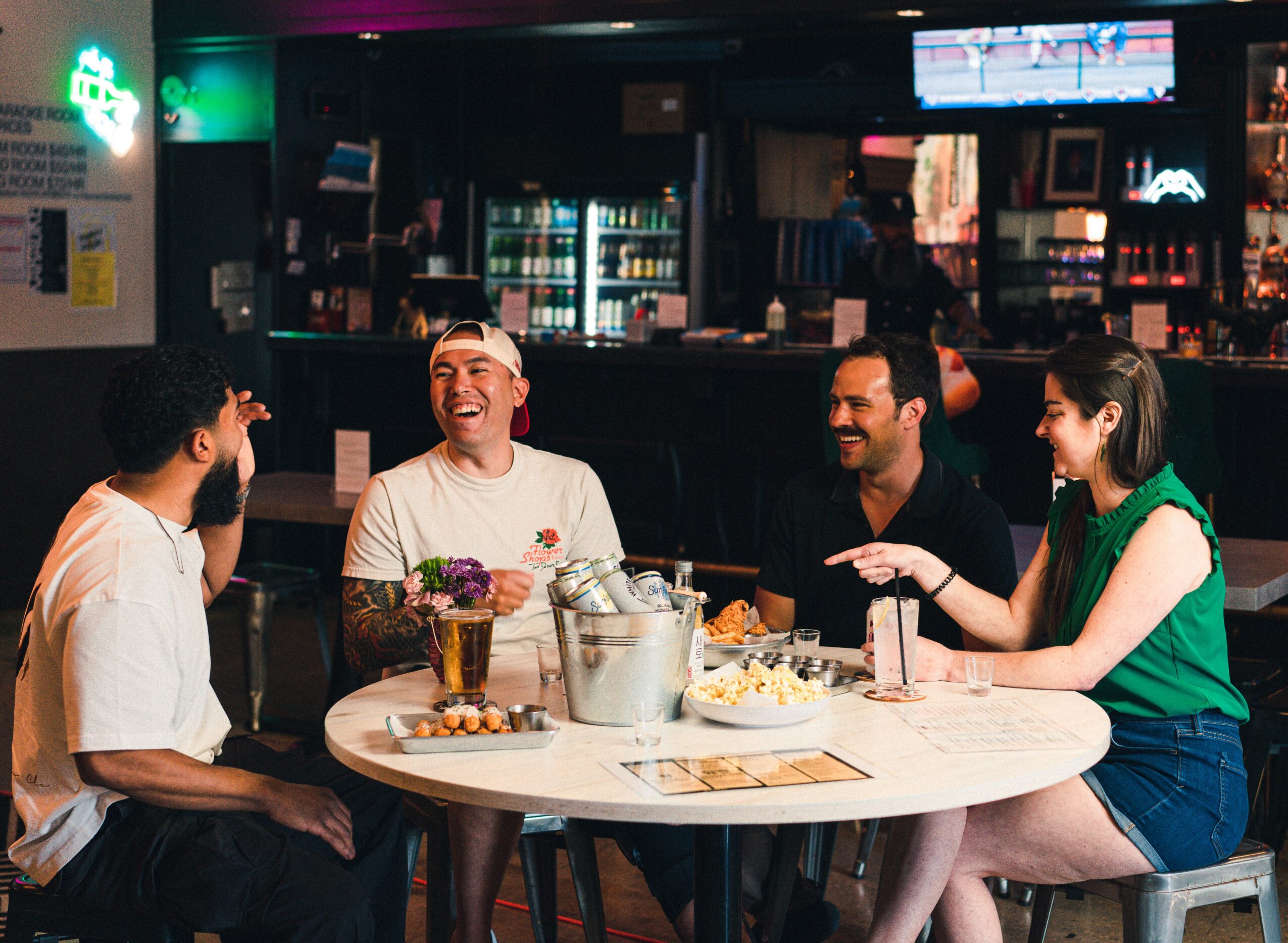 Four people sitting around a table laughing and talking in a bar or pub setting.
