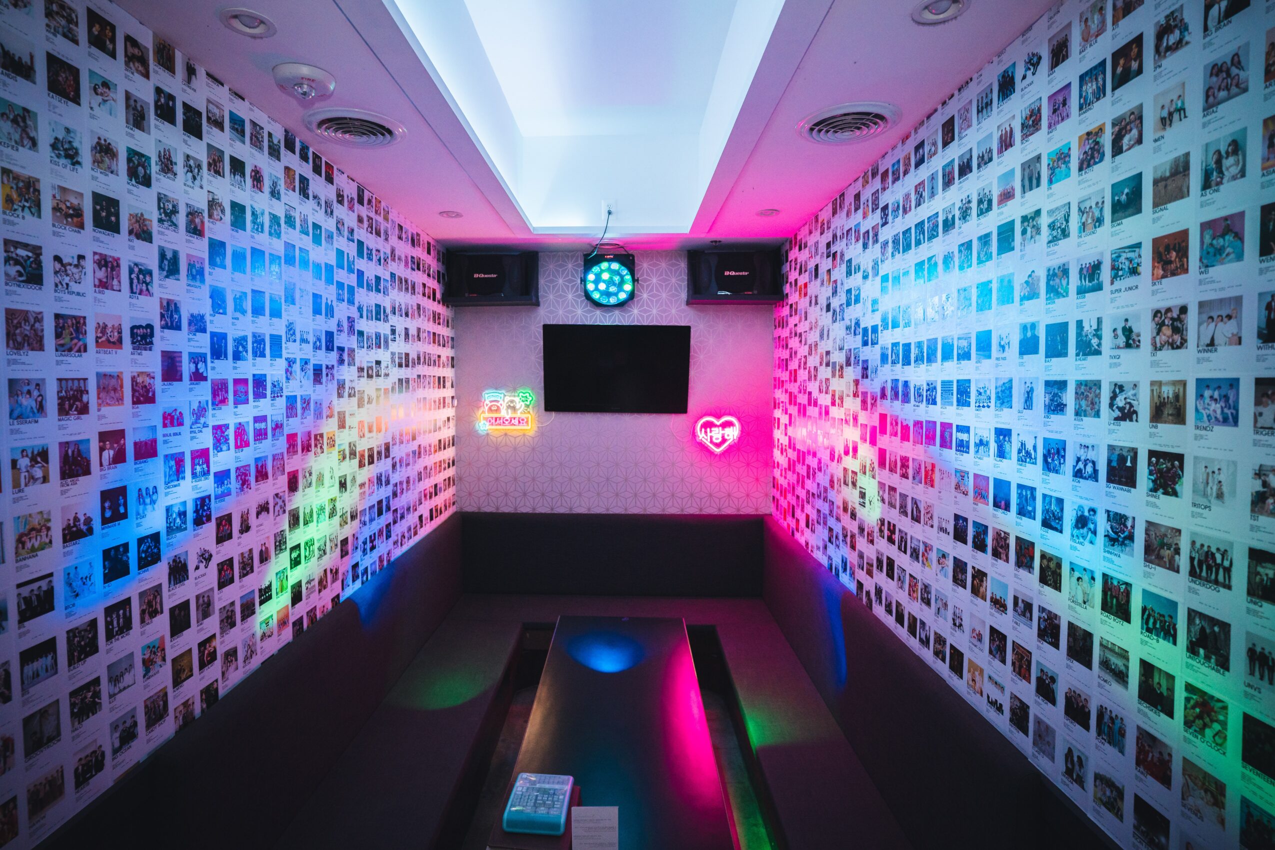 Room with walls covered in small photos, colorful lighting, and a large screen on the back wall.