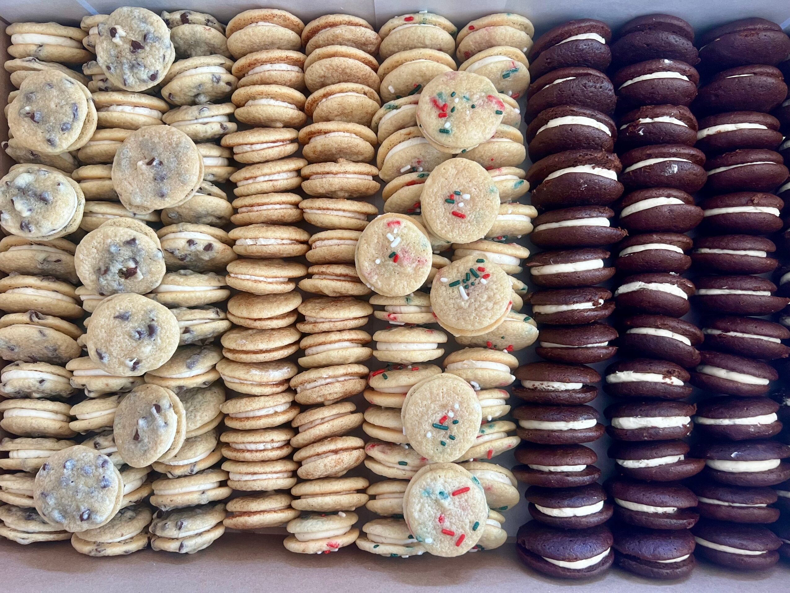 Rows of assorted cookies and macarons arranged vertically, with different colors and toppings, on a flat surface.