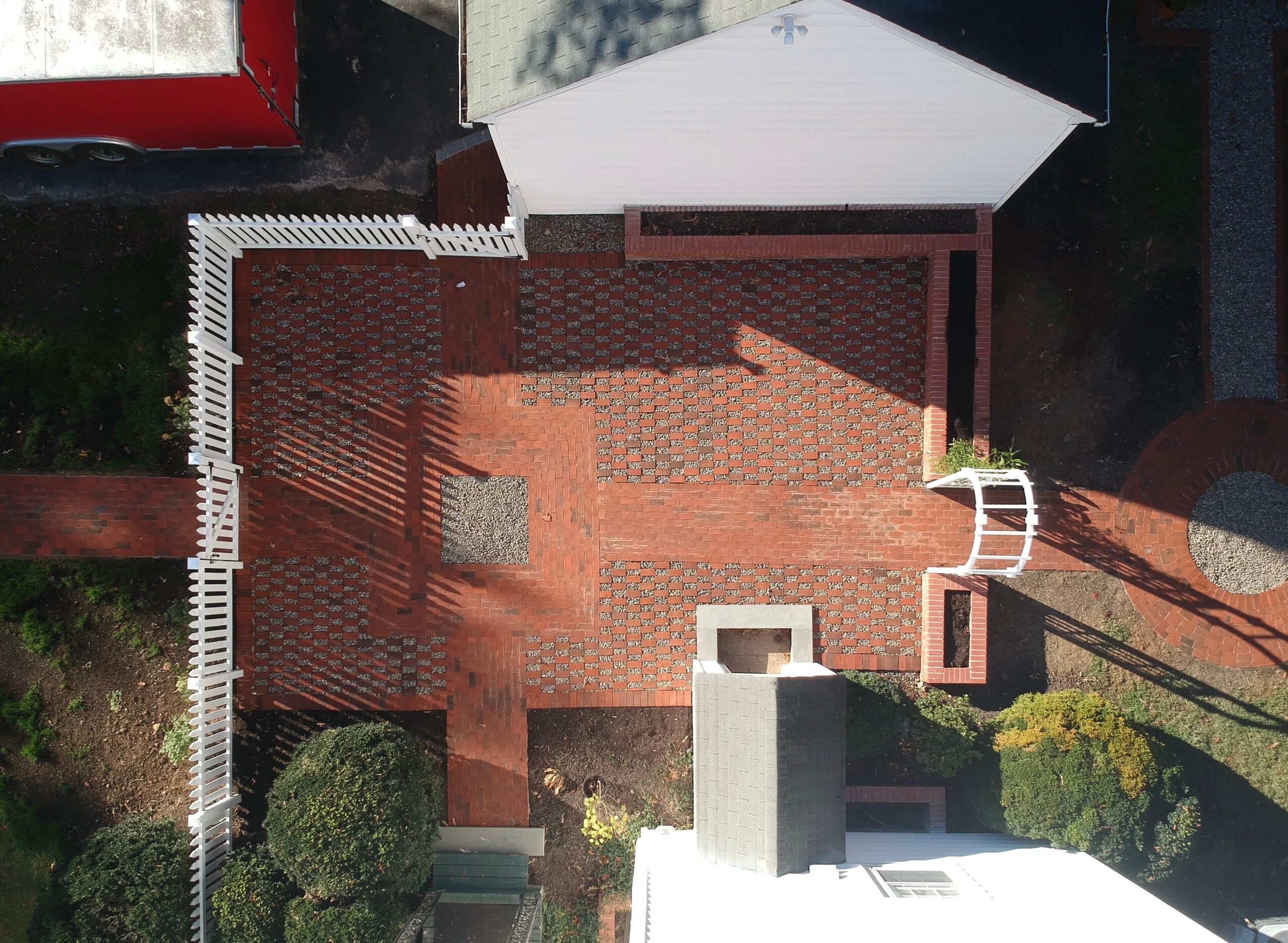 A brick patio with a small table and chairs, surrounded by greenery and structures, viewed from above.