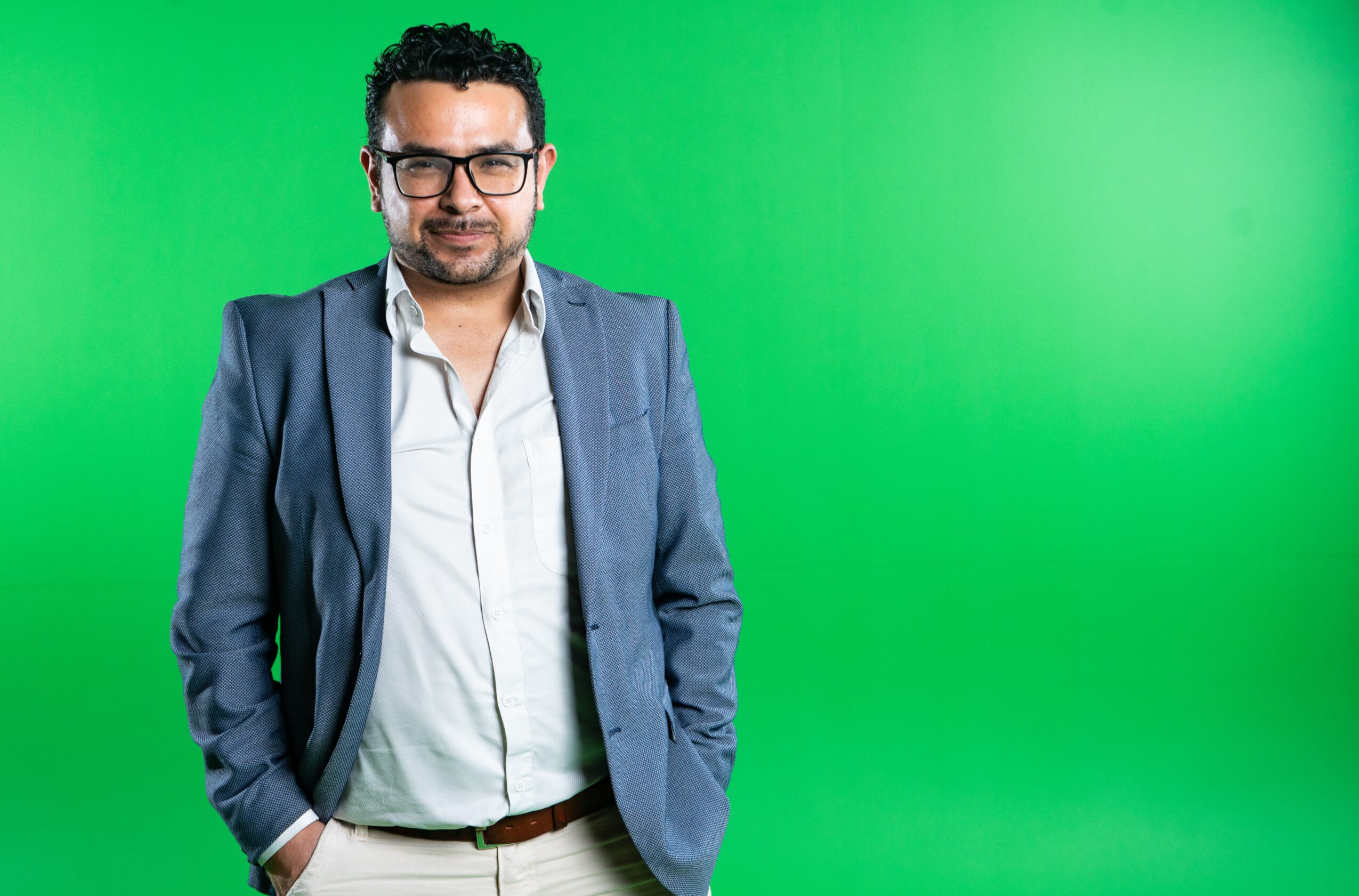 Man with glasses in a suit standing against a green background.