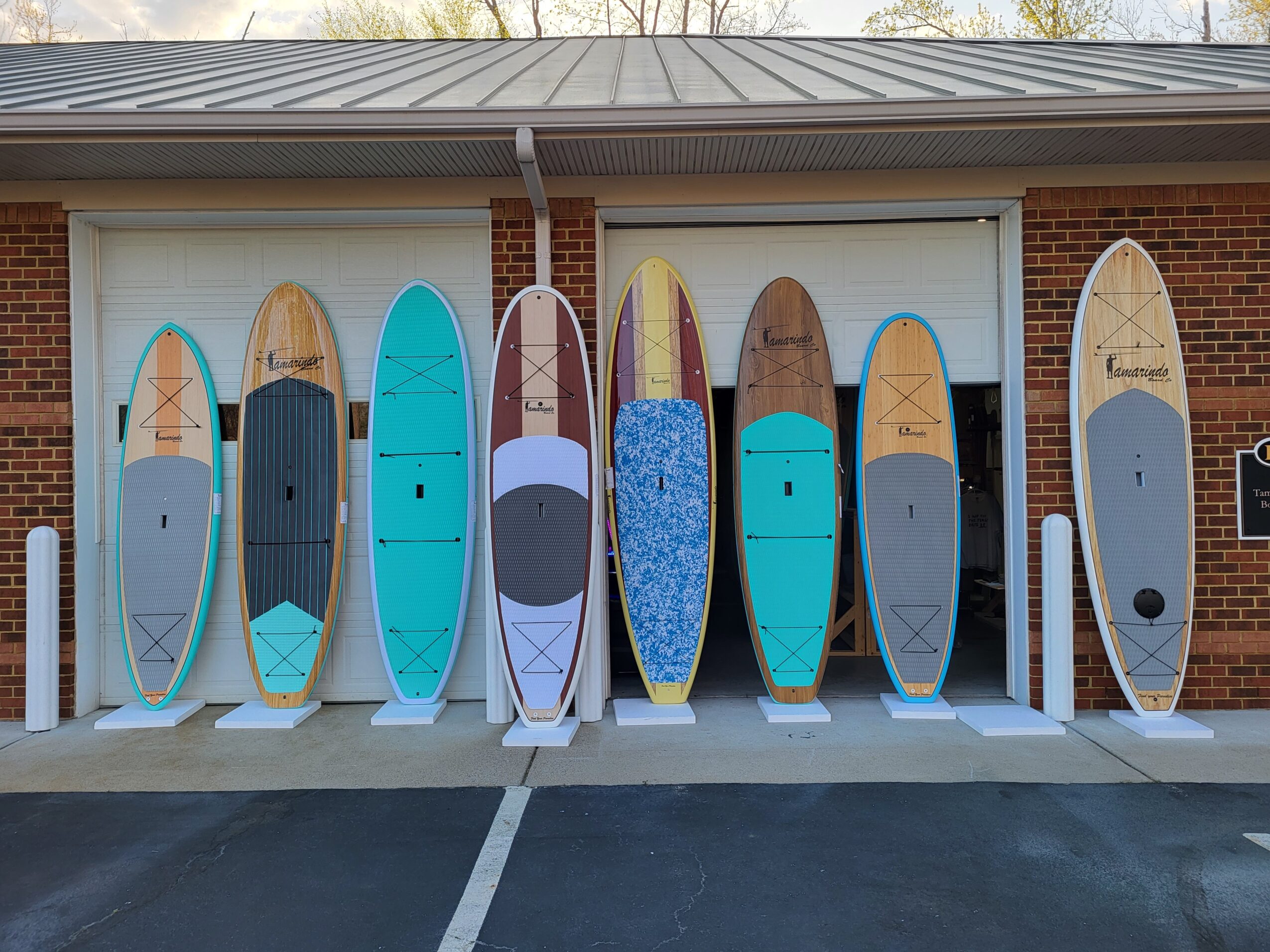 Multiple surfboards leaning against a garage door, with a brick building and trees in the background.