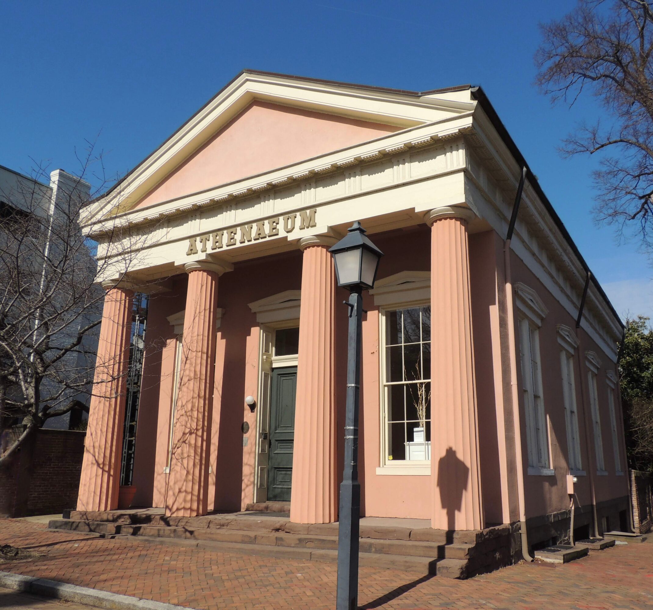 Pink building with columns and a triangular pediment, labeled 'THEATRE' above the entrance, under a clear blue sky.