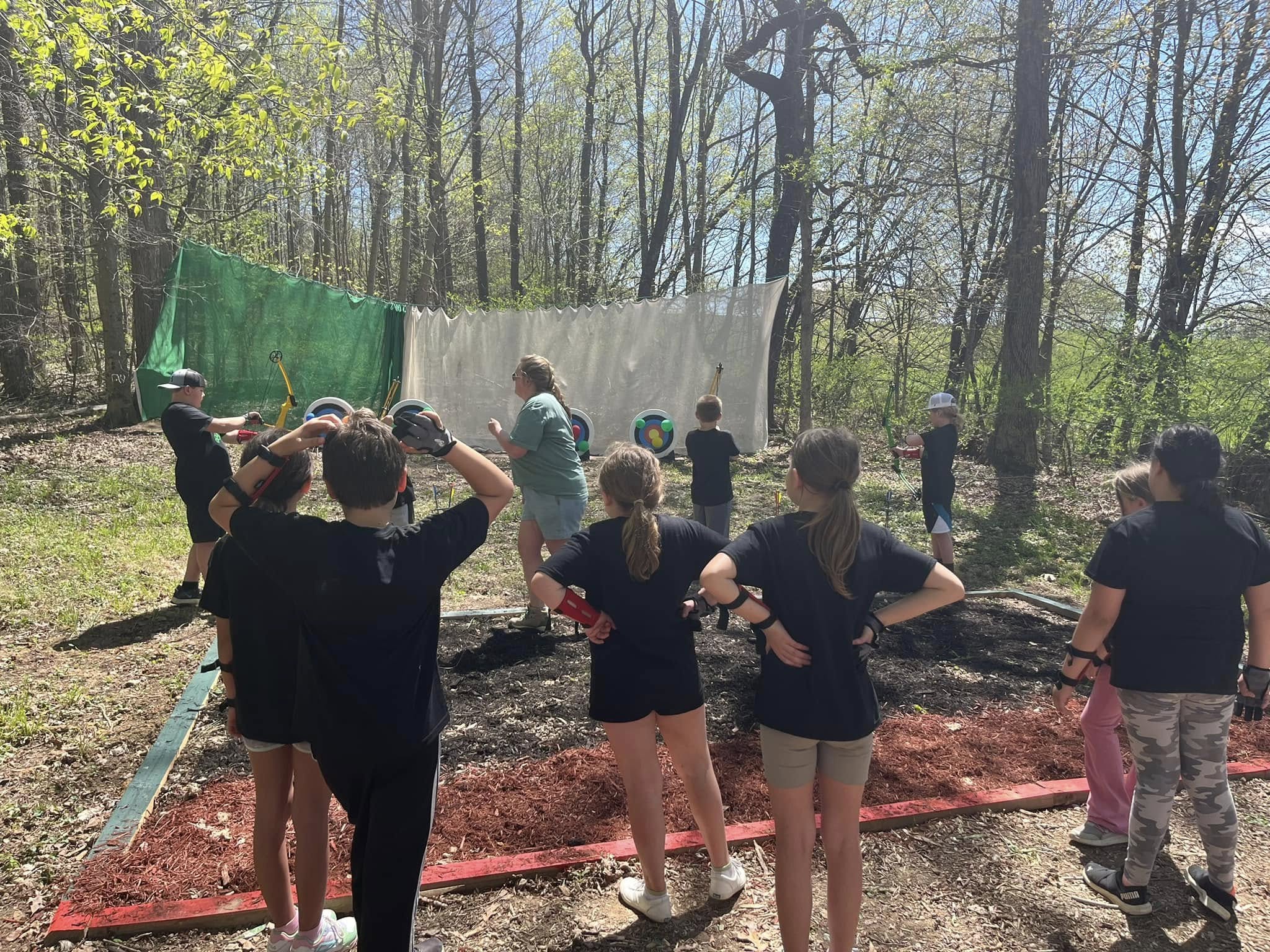 Group of children outdoors near trees, some holding hands, with laundry hanging on a line behind them.