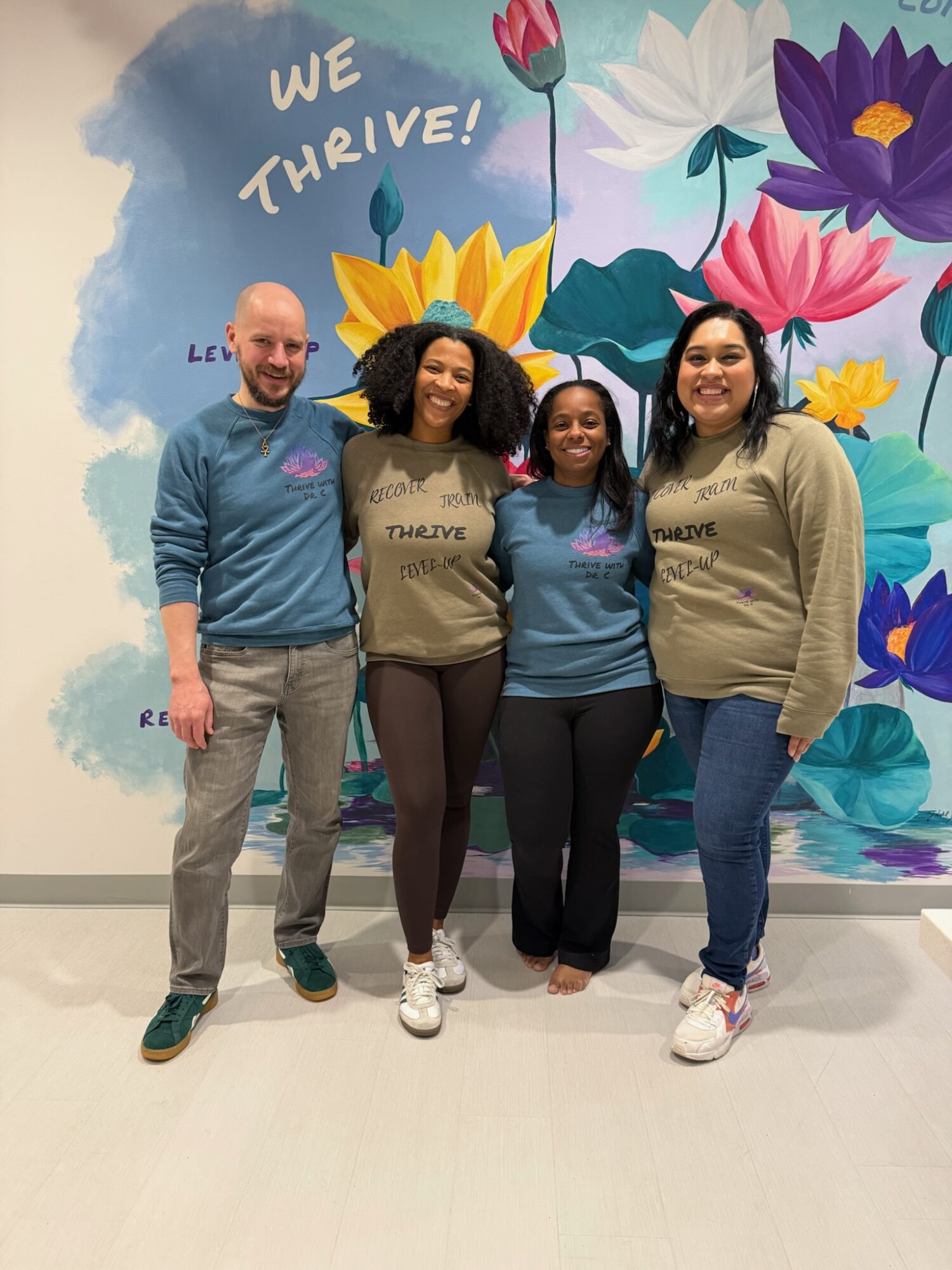 Four people stand in front of a colorful floral mural with the words