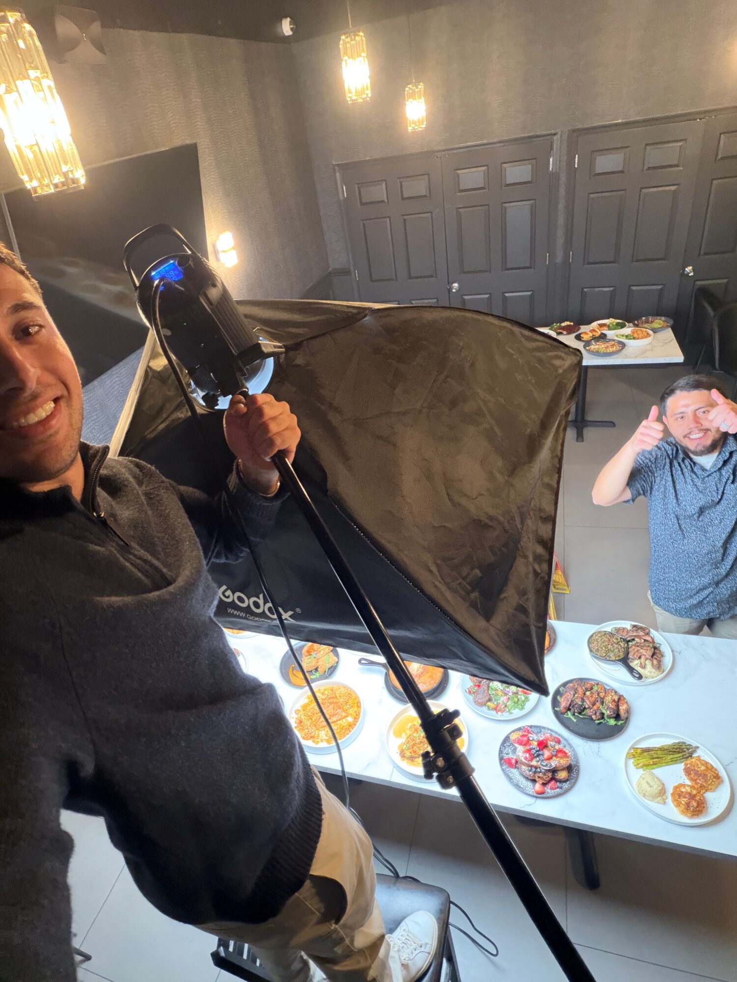 Person taking a photo with a camera, with a table of food and another person in the background.