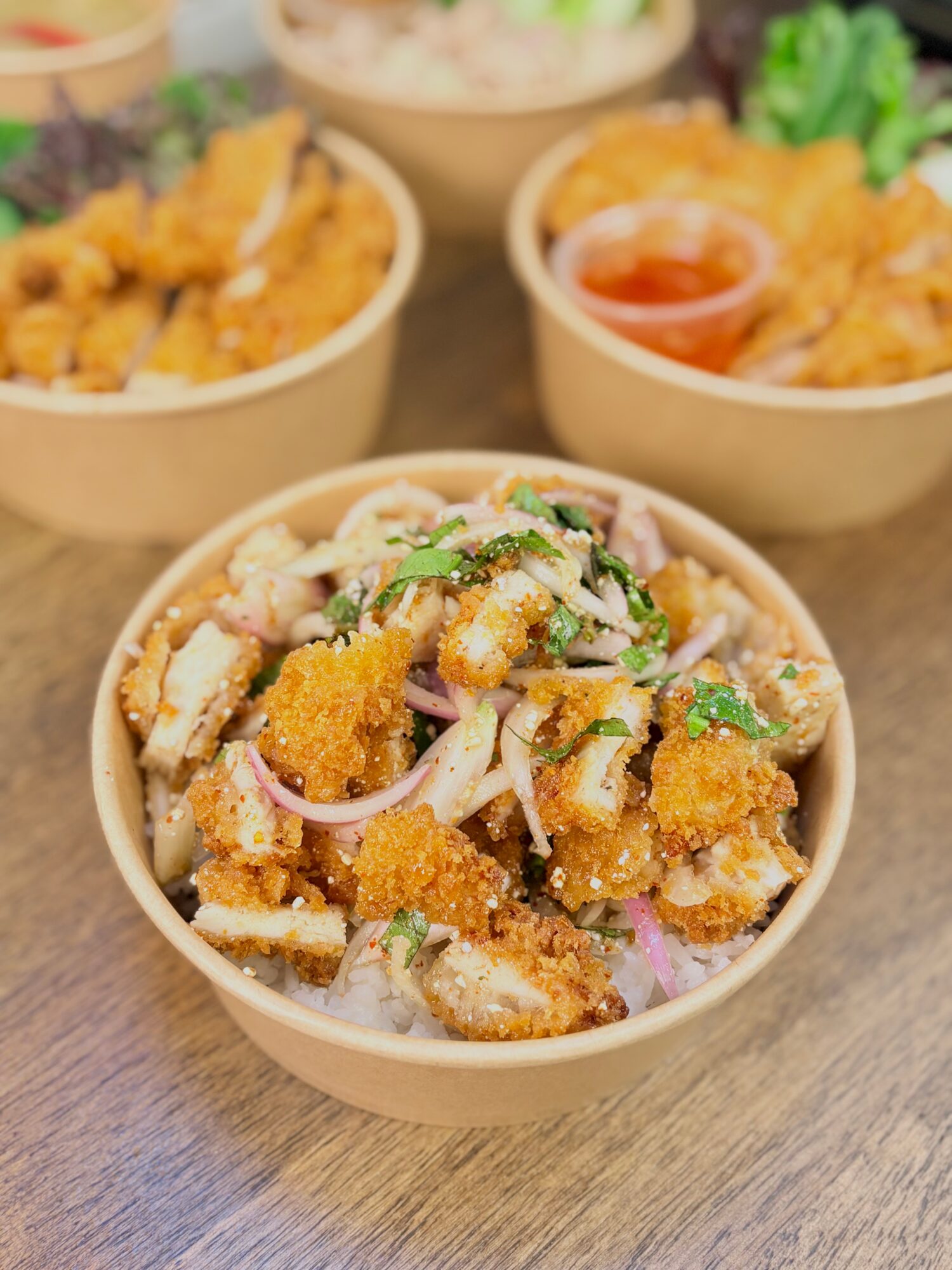 Bowl of fried chicken pieces with onions and herbs, with two other bowls of fried food and sauce in background