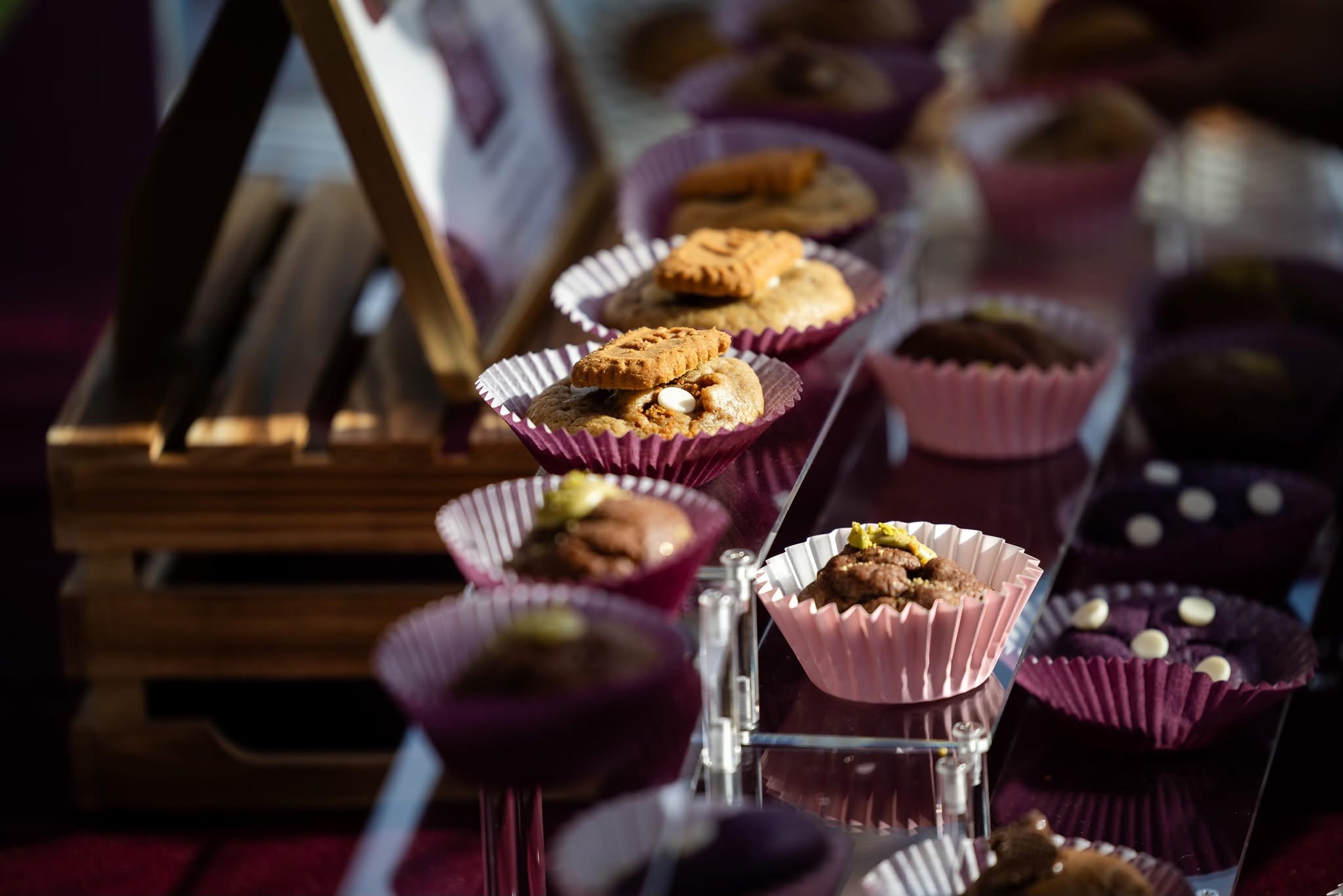 Assorted cookies and baked goods displayed on a table with pink and purple cupcake liners, some in glass containers.