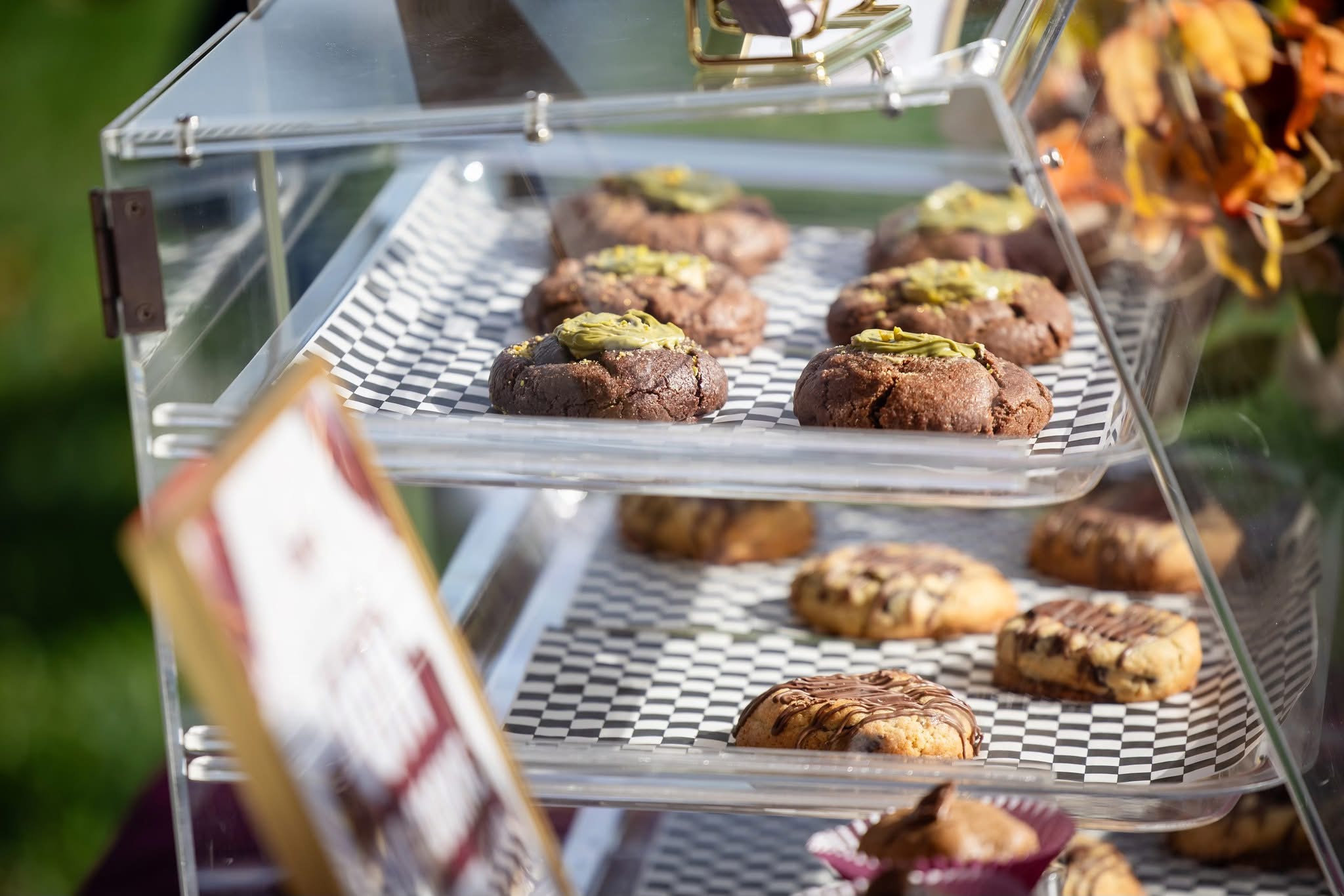 Display case with various cookies and baked goods on metal trays, some topped with green icing or sprinkles.