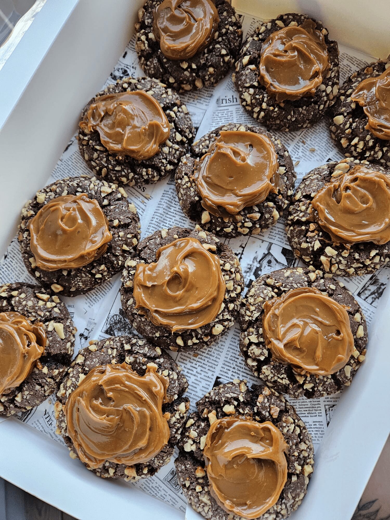 Chocolate cookies topped with caramel and sprinkled with chopped nuts, arranged in a white tray.