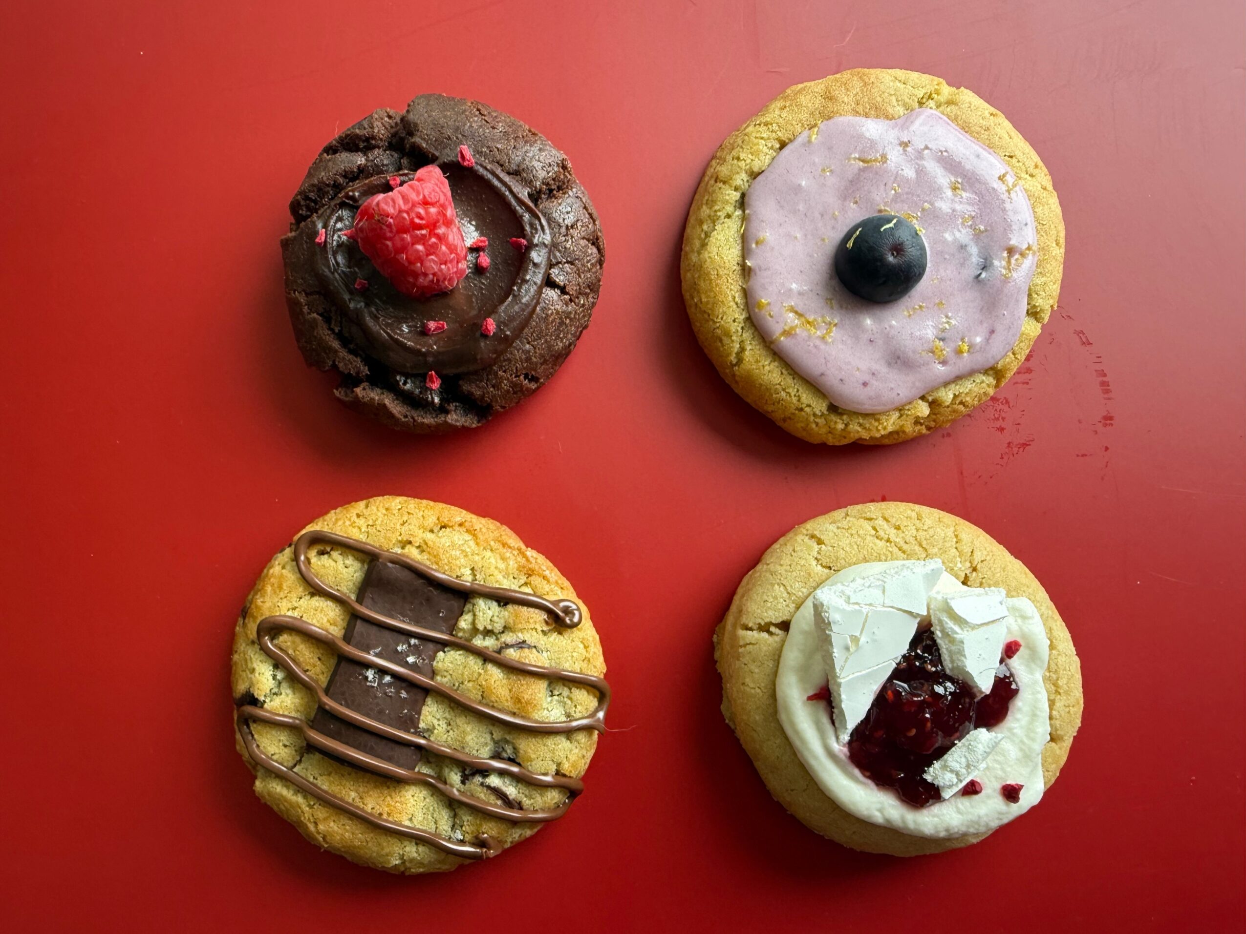 Four decorated cookies on a red surface, each with different toppings and designs.