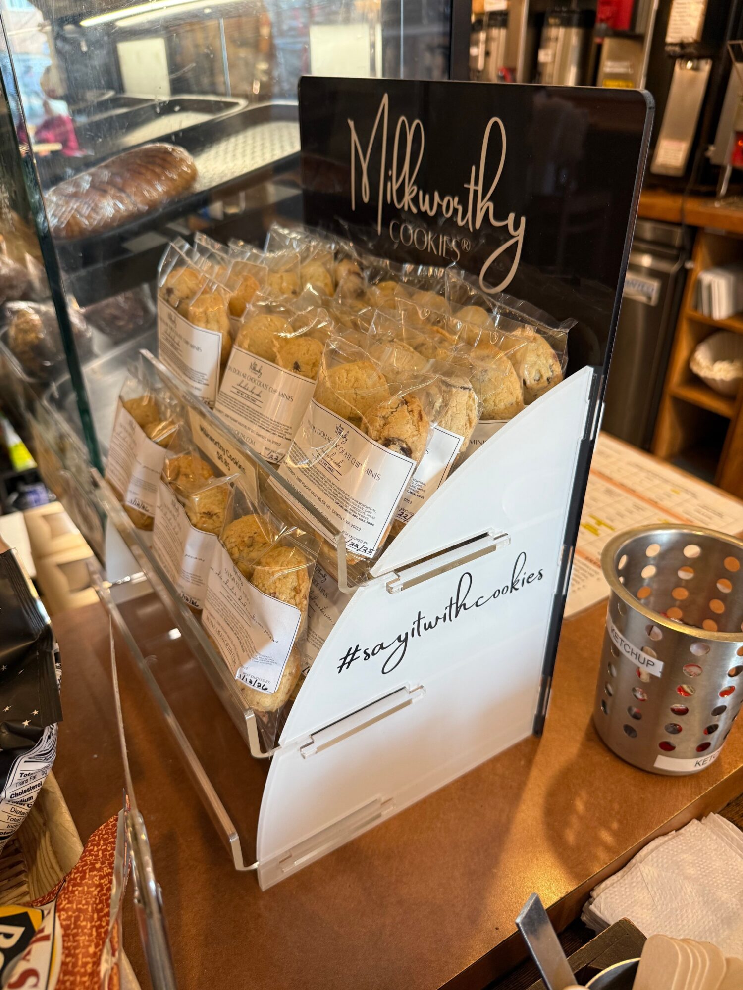 Display case with cookies and a sign, on a wooden table with various items, in a store setting.