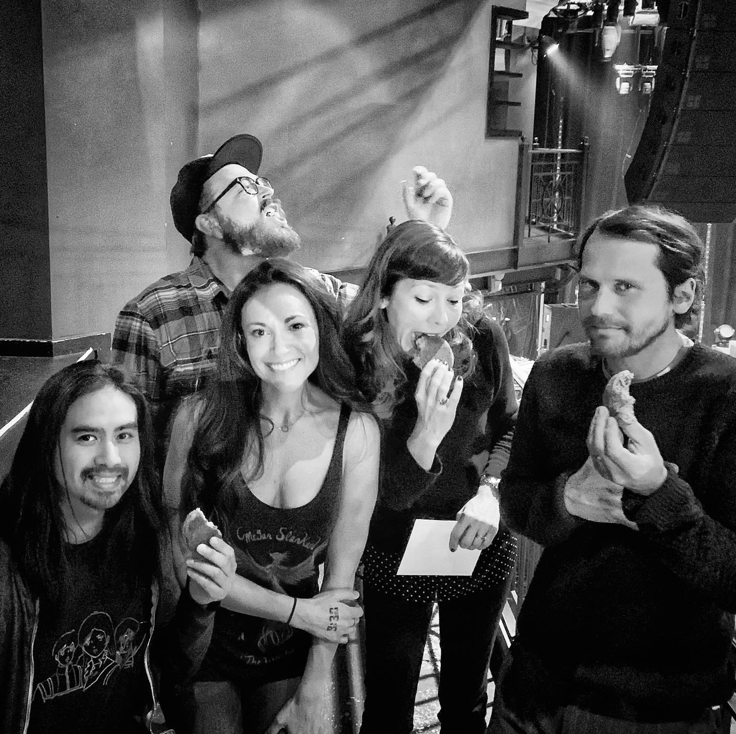 Group of five people smiling and eating in a room with stairs in the background.