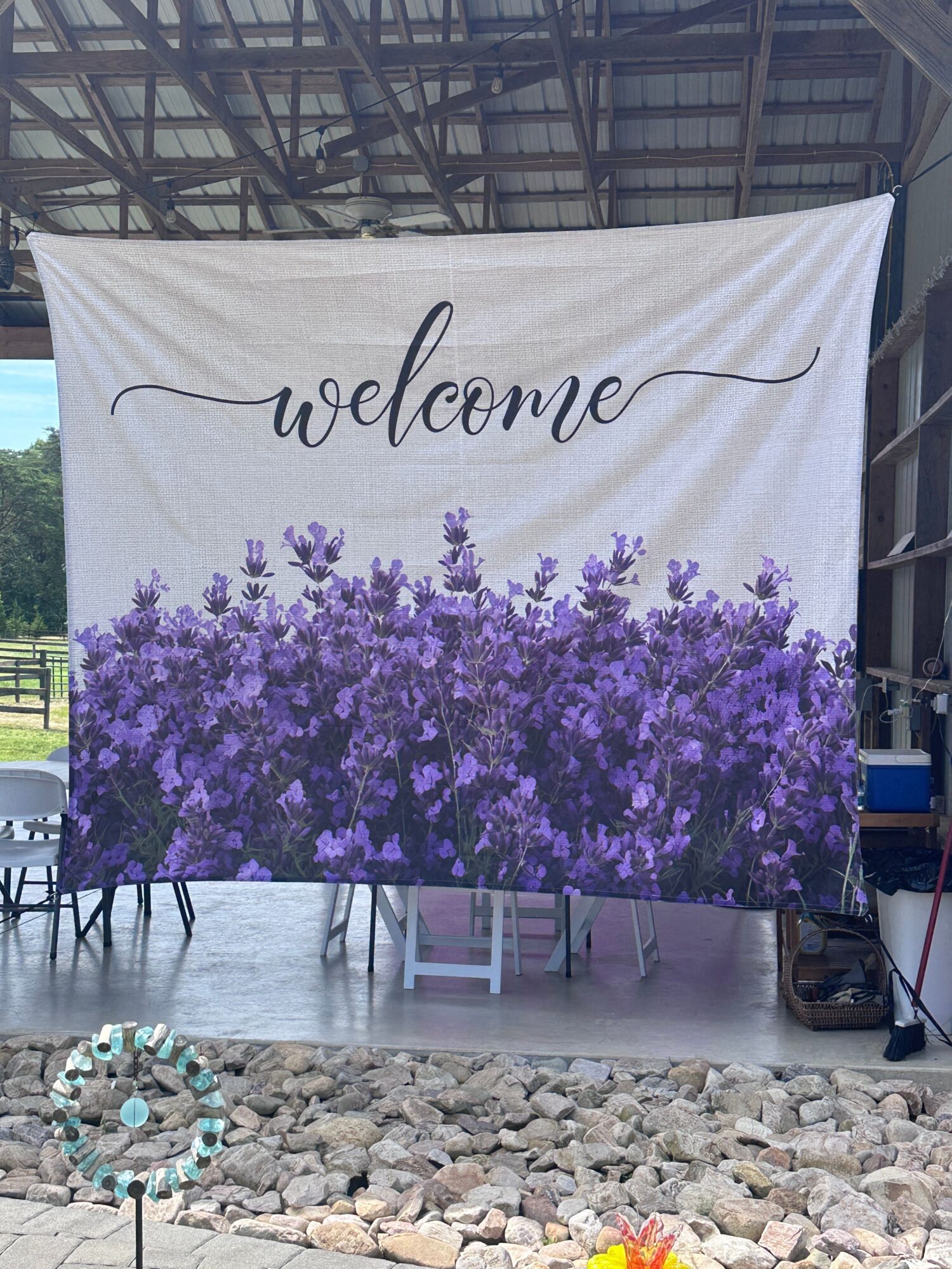A fabric banner with a purple flowering tree and the word 'welcome' written in cursive, hanging outdoors on a metal frame.