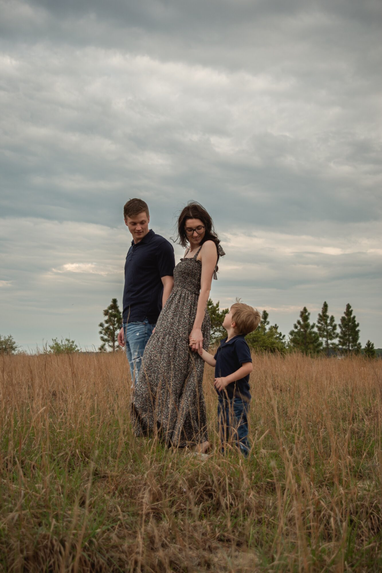 Three people standing in a grassy field under cloudy sky, with trees in the background.