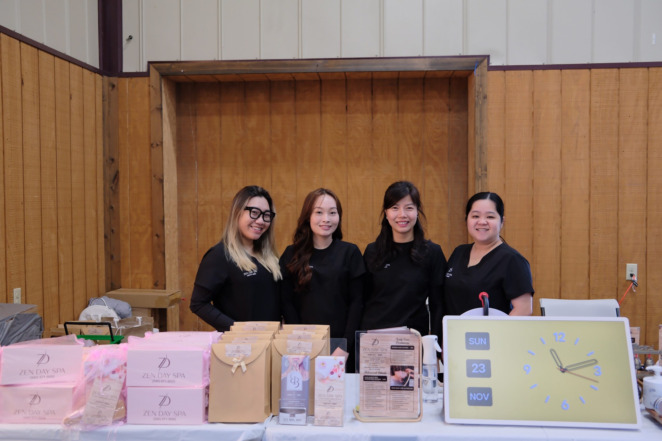 Four women standing together indoors, smiling, with wooden wall background.