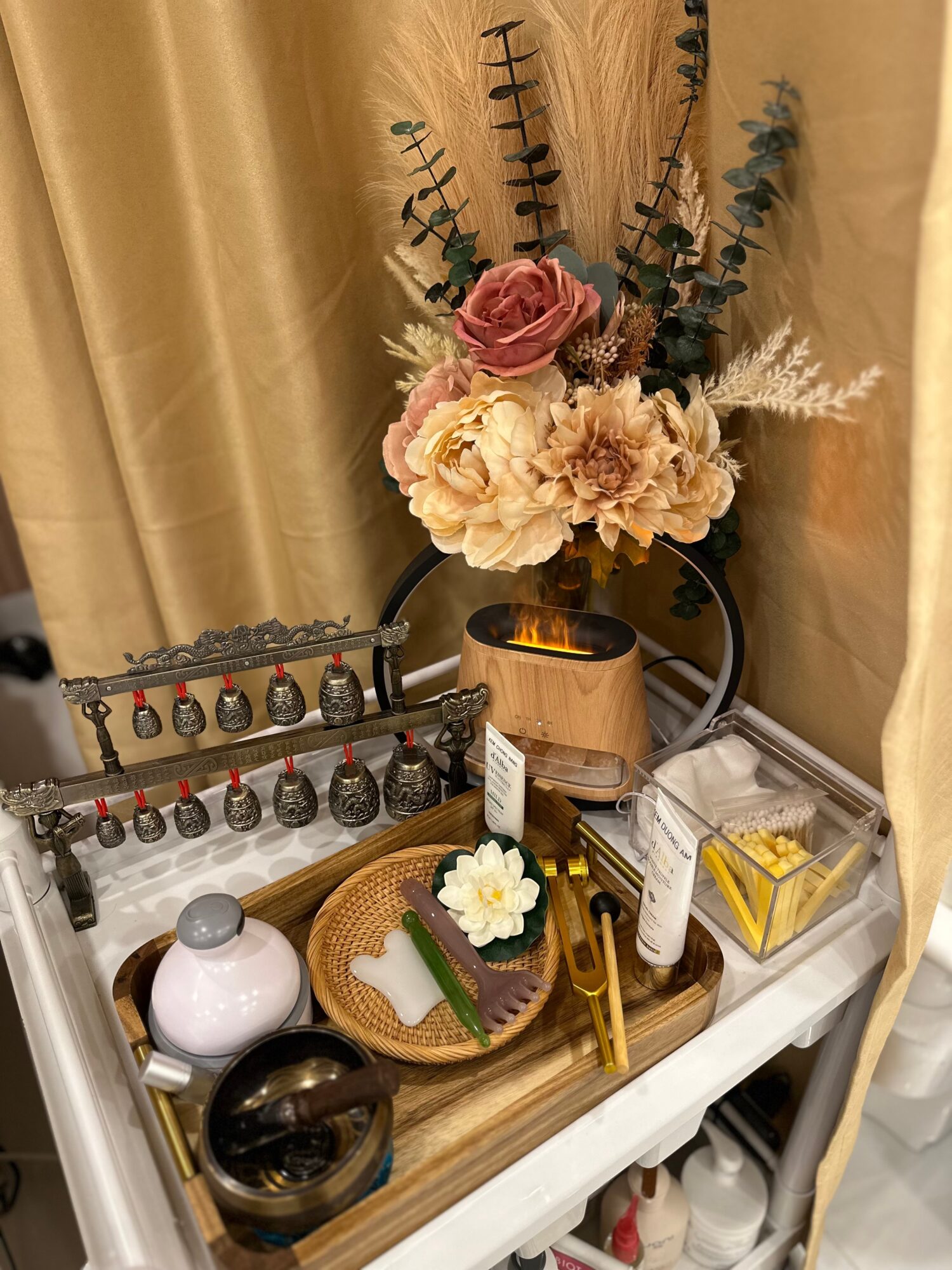 Flower arrangement with pink and white flowers, dried foliage, on a white table with decorative items and a curtain background.
