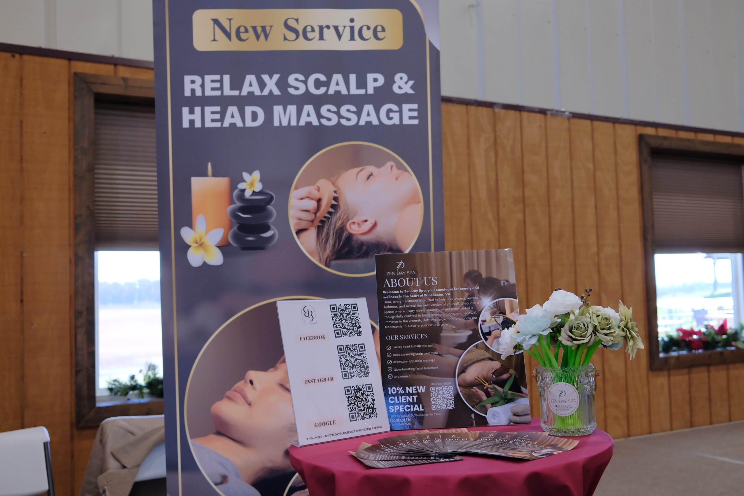 A promotional stand for scalp and head massage services with a photo of a woman receiving a massage, a QR code, and a flower arrangement on a table.
