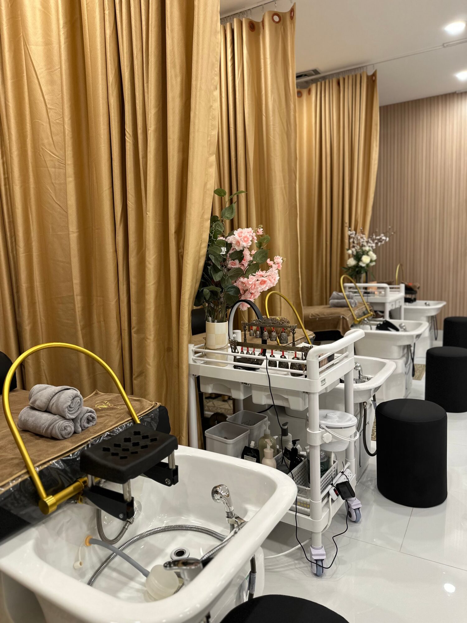 Salon with gold curtains, white furniture, flower arrangements, and black stools, viewed from the side. Word count: 20.