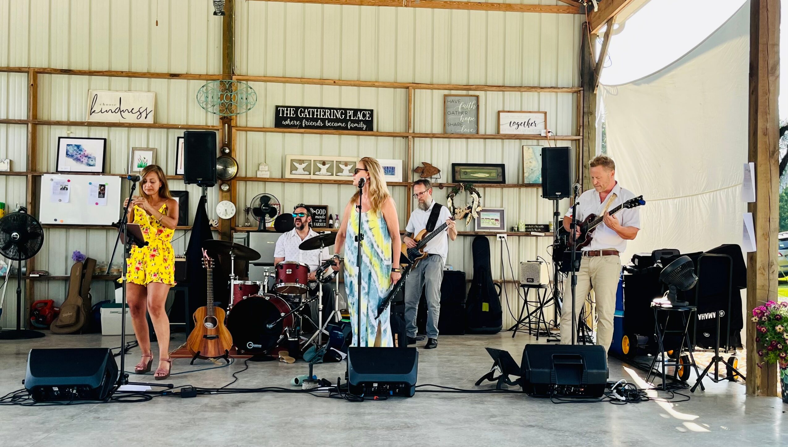 Band performing on stage with five members, instruments, and sound equipment inside a rustic venue.