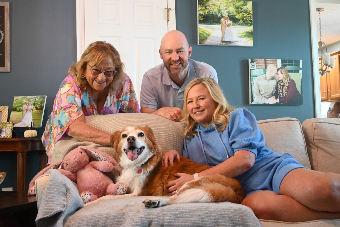 Four people and a dog on a sofa in a living room, smiling and relaxing together.