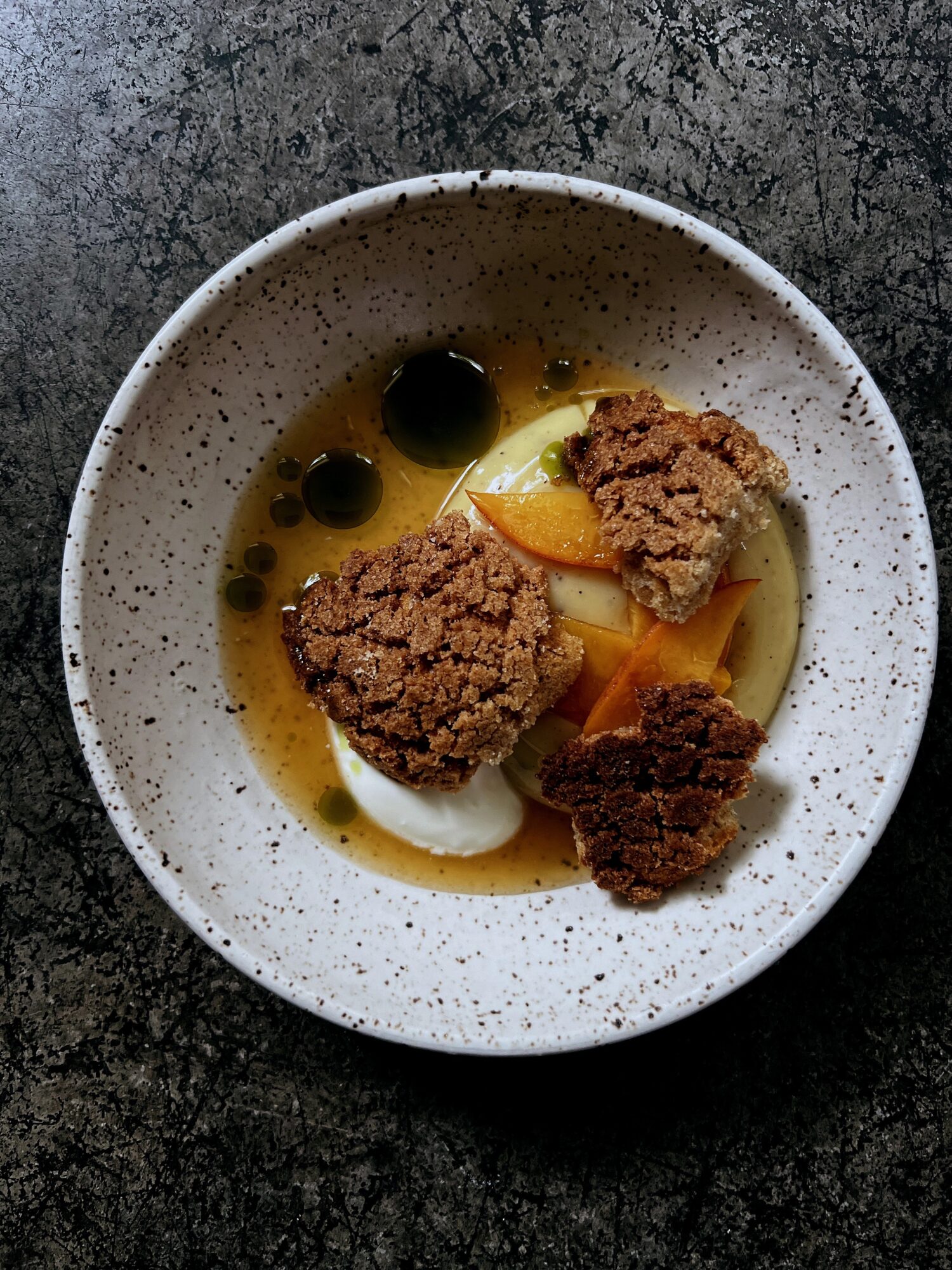 Bowl with fried food, yellow sauce, black olives, and lemon wedge on dark surface.