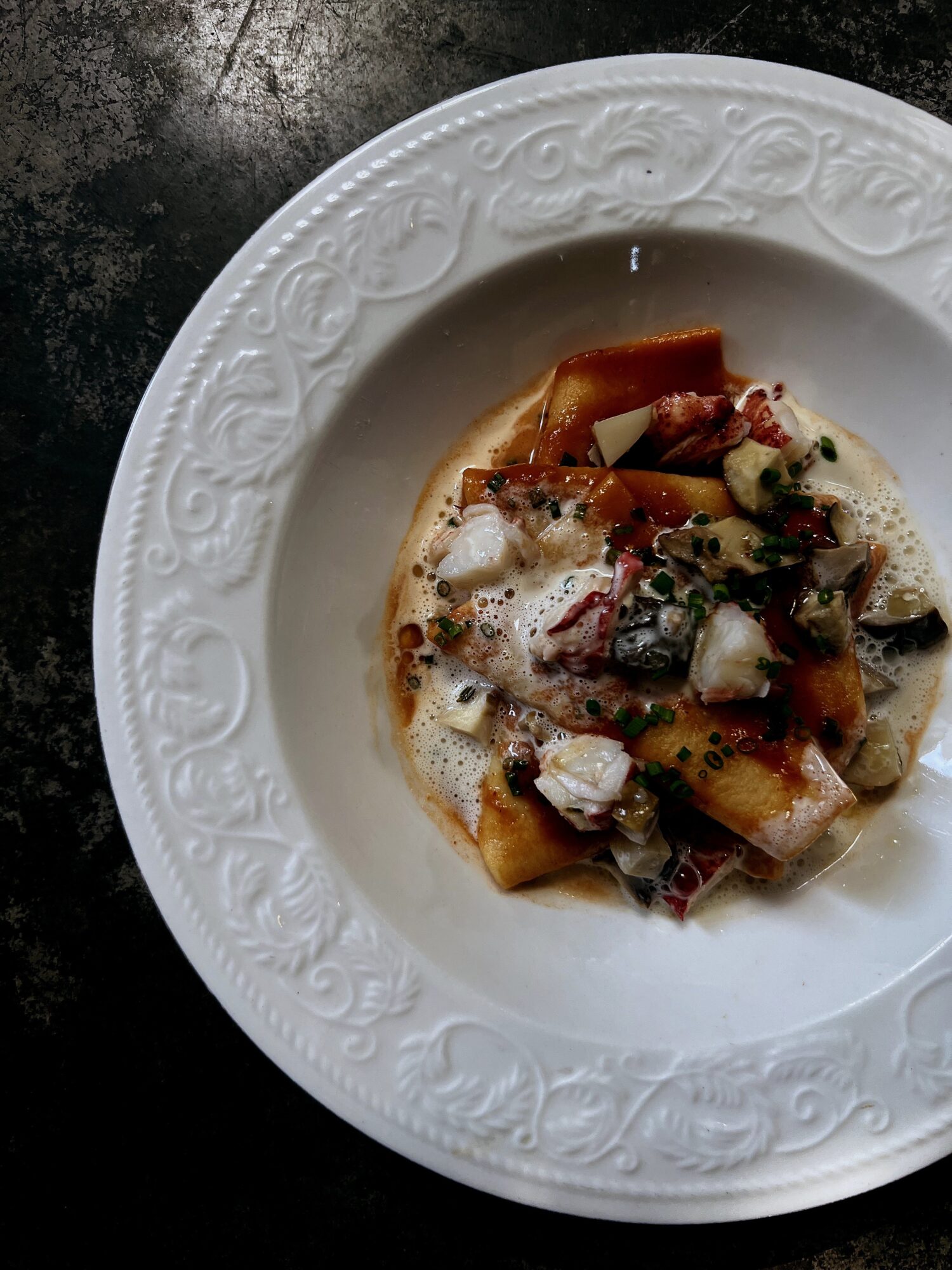 Pasta dish with sauce, cheese, and herbs on a decorative white plate, viewed from above.