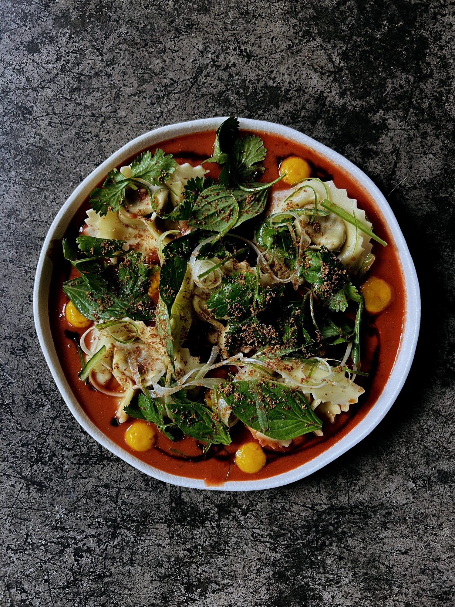 Bowl of salad with mixed greens, cherry tomatoes, and dressing on a dark surface.