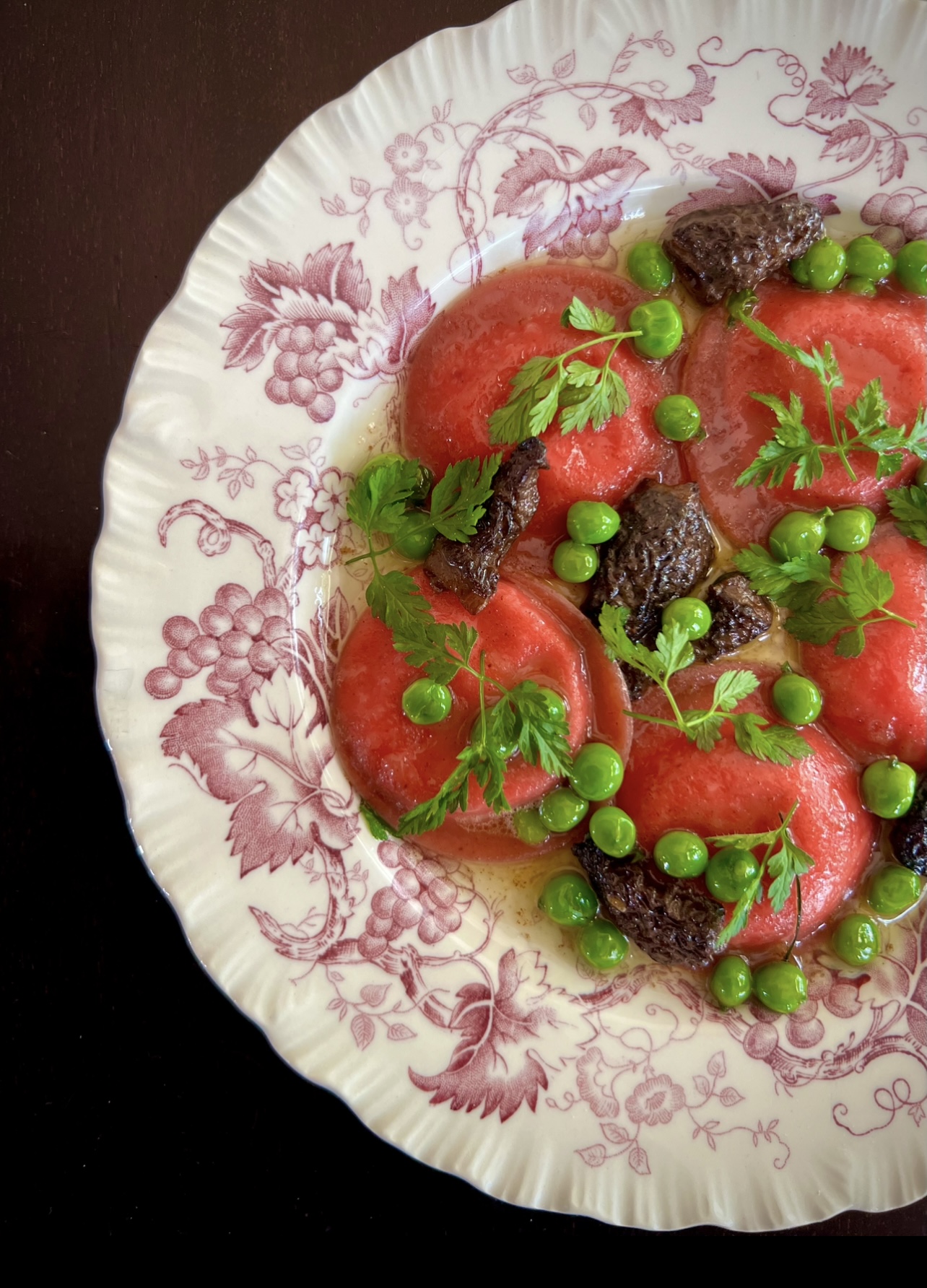 Salad with tomato slices, green peas, herbs, and dark toppings on a floral-patterned plate.