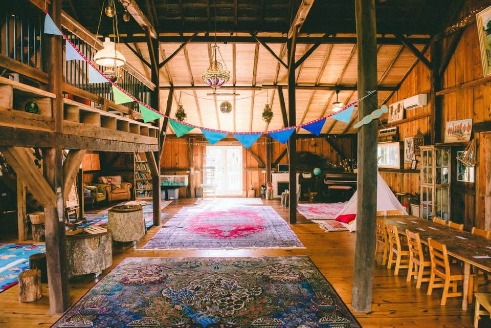 Interior of a rustic wooden building with bookshelves, tables, and colorful bunting, illuminated by natural light from windows.