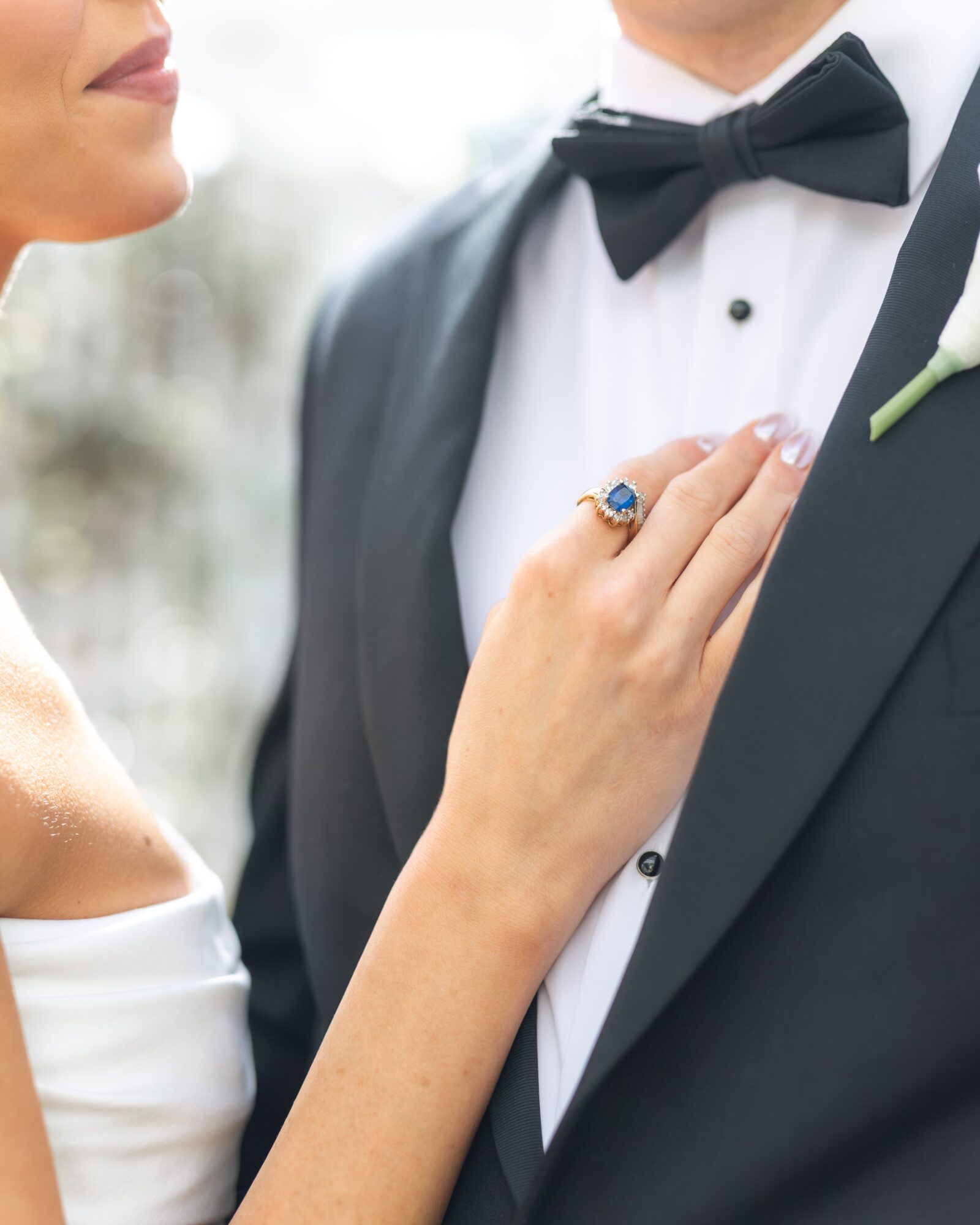 Close-up of a woman touching a man's tuxedo, showing her hand with a ring, at a formal event.